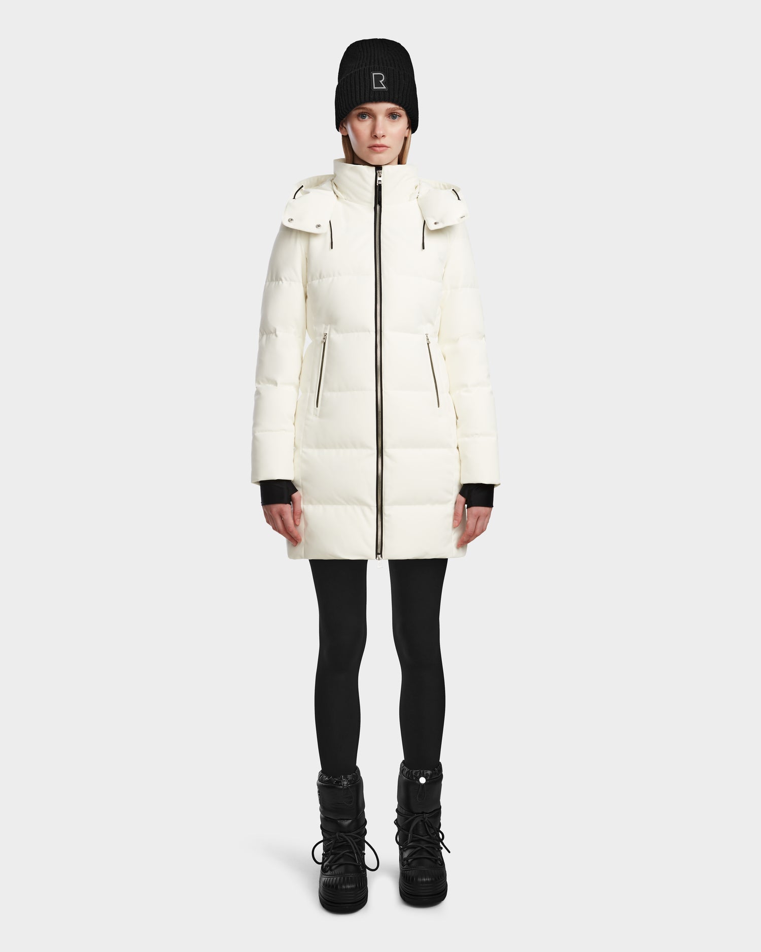 A person wears the Rudsak MIRIAM - L123544 Iceland womens down puffer, paired with a black beanie, black leggings, and black winter boots, standing facing forward against a plain white background.
