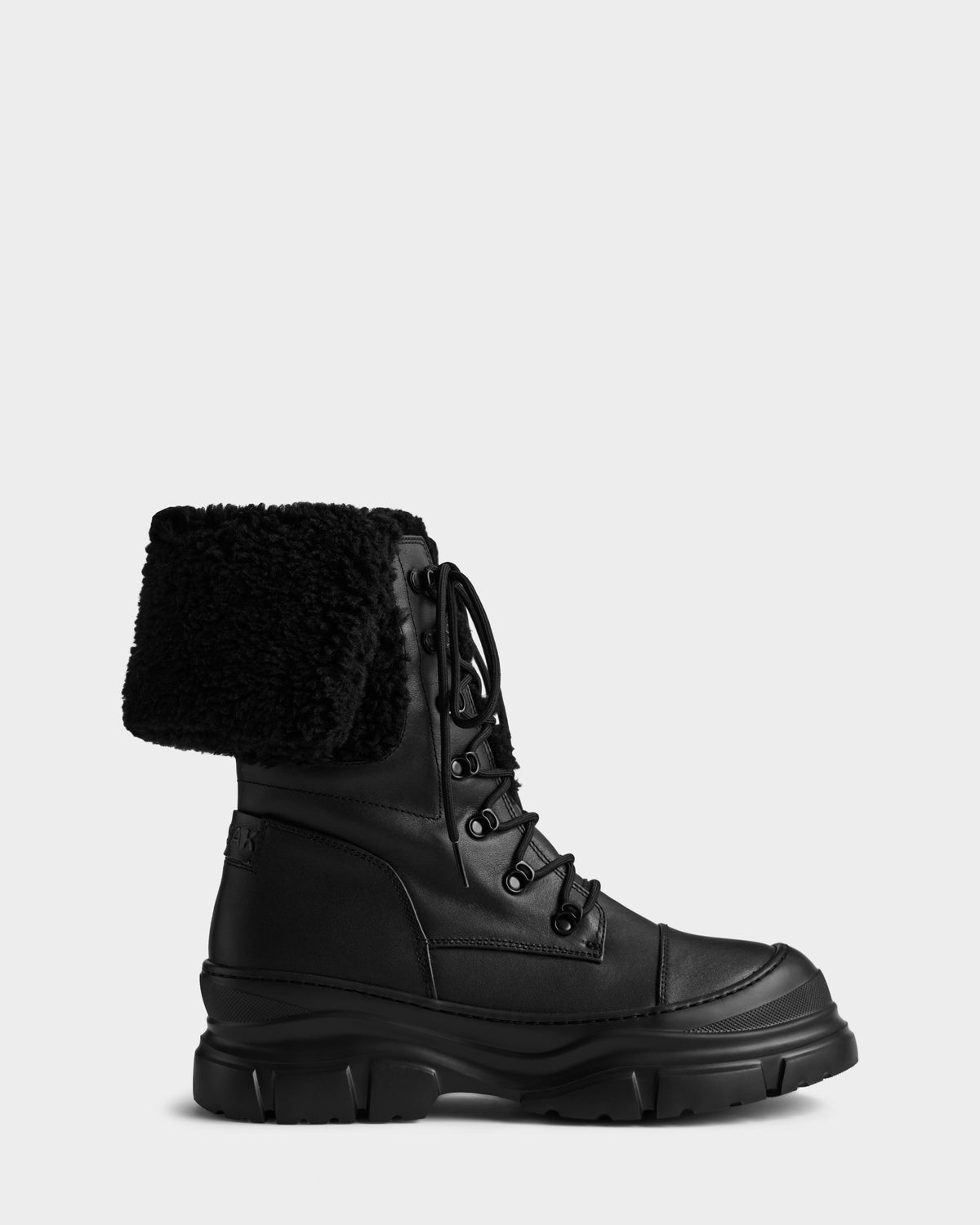 The MODENA - 8225024 Black by Rudsak is a black leather combat winter boot with a thick, rugged sole, laces, and a folded-over black faux shearling cuff, shown against a plain light background.