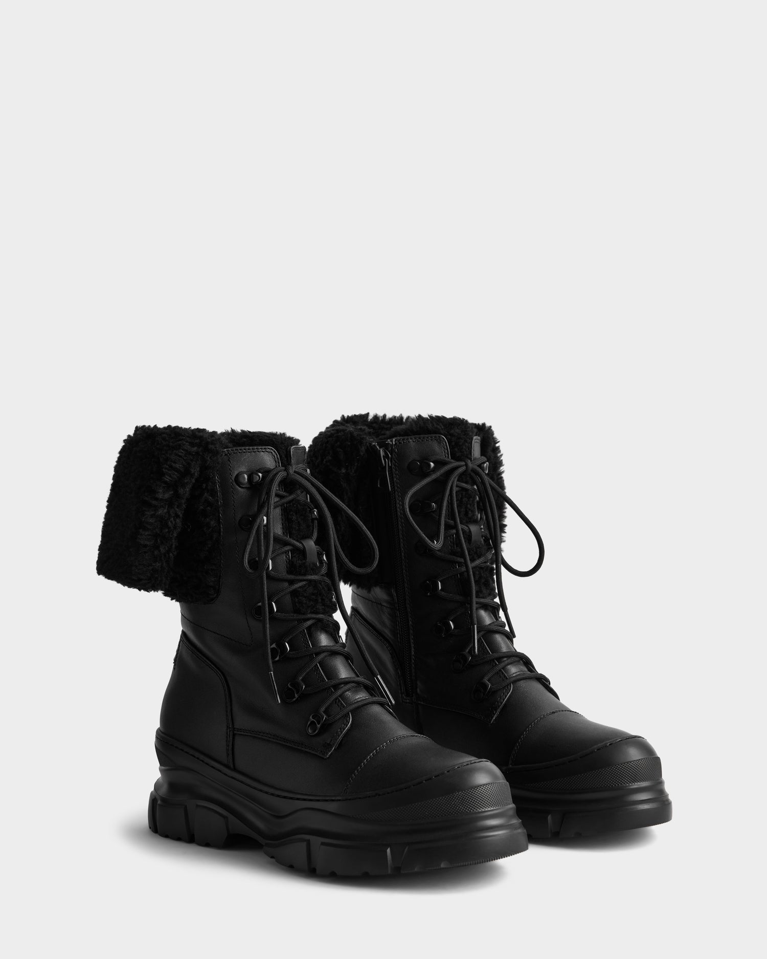 The MODENA - 8225024 Black winter boots by Rudsak feature lace-up fronts, thick textured soles, and folded faux shearling cuffs, shown against a plain light gray background.