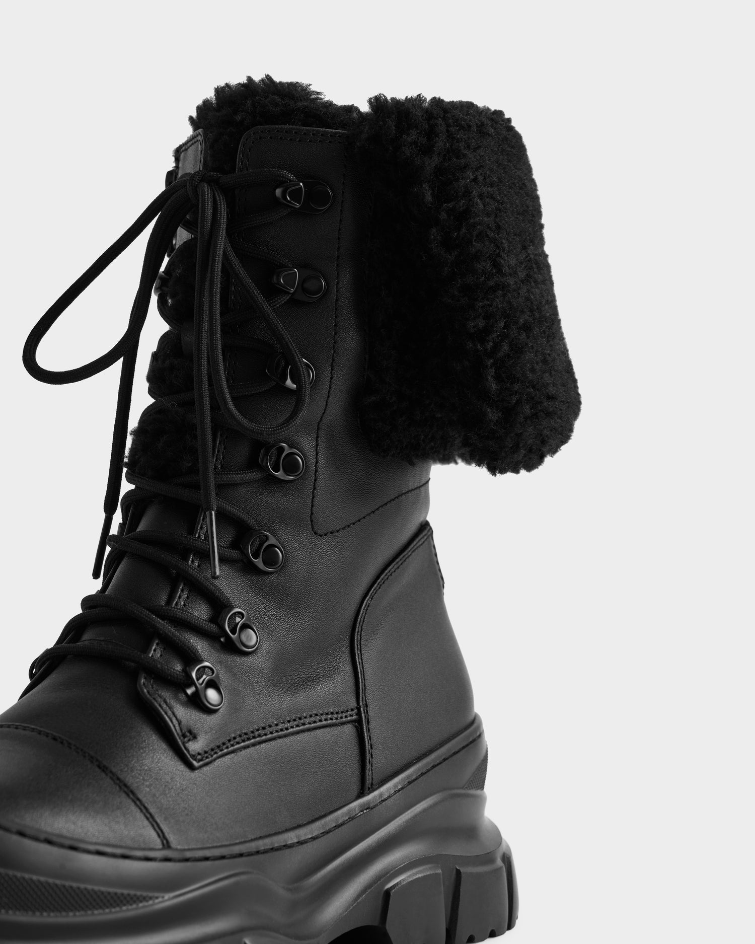 A close-up of the Rudsak MODENA - 8225024 Black boot, featuring black leather, a chunky sole, and a folded-down faux shearling collar—ideal for winter—set against a plain white background.