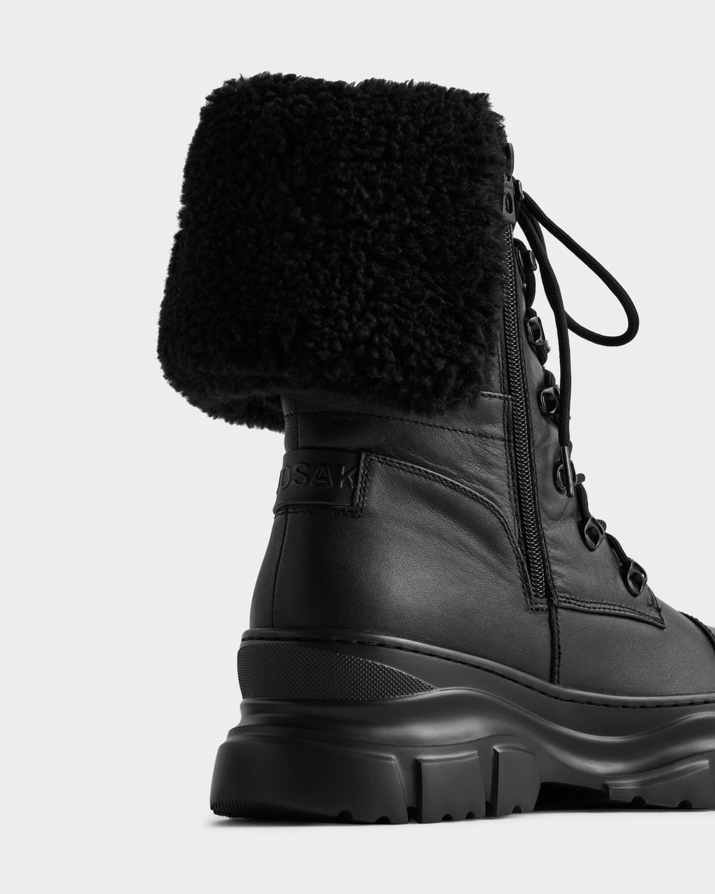 The MODENA - 8225024 Black by Rudsak is a black leather boot featuring a side zipper, thick treaded sole, and folded faux shearling collar. The brand's name is embossed on the heel. Shown on a plain white background.