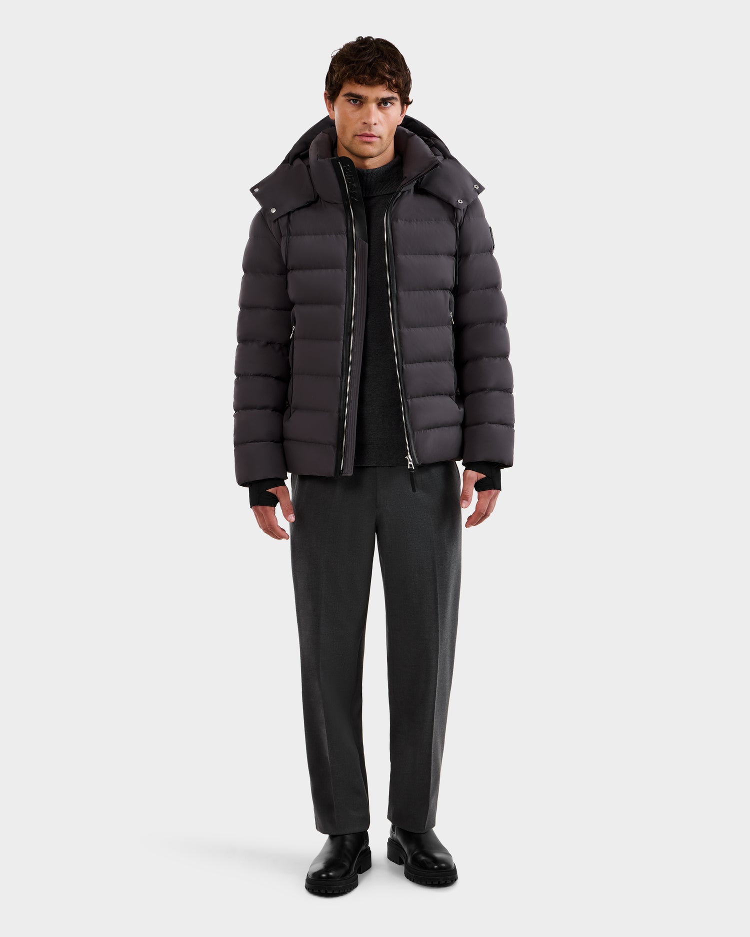 A man faces forward wearing the Rudsak NAVAN - 6125598 Grey men's quilted down puffer over a black top, gray pants, and black shoes against a plain white background.