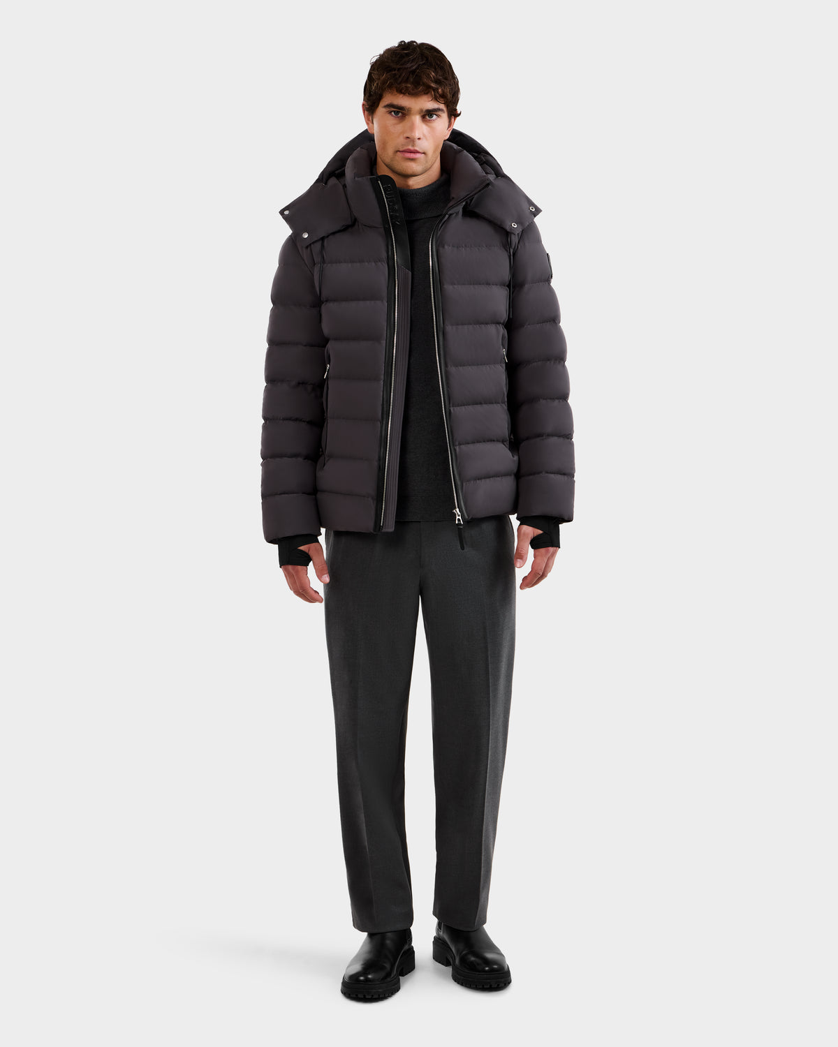 A man faces forward wearing the Rudsak NAVAN - 6125598 Grey men's quilted down puffer over a black top, gray pants, and black shoes against a plain white background.