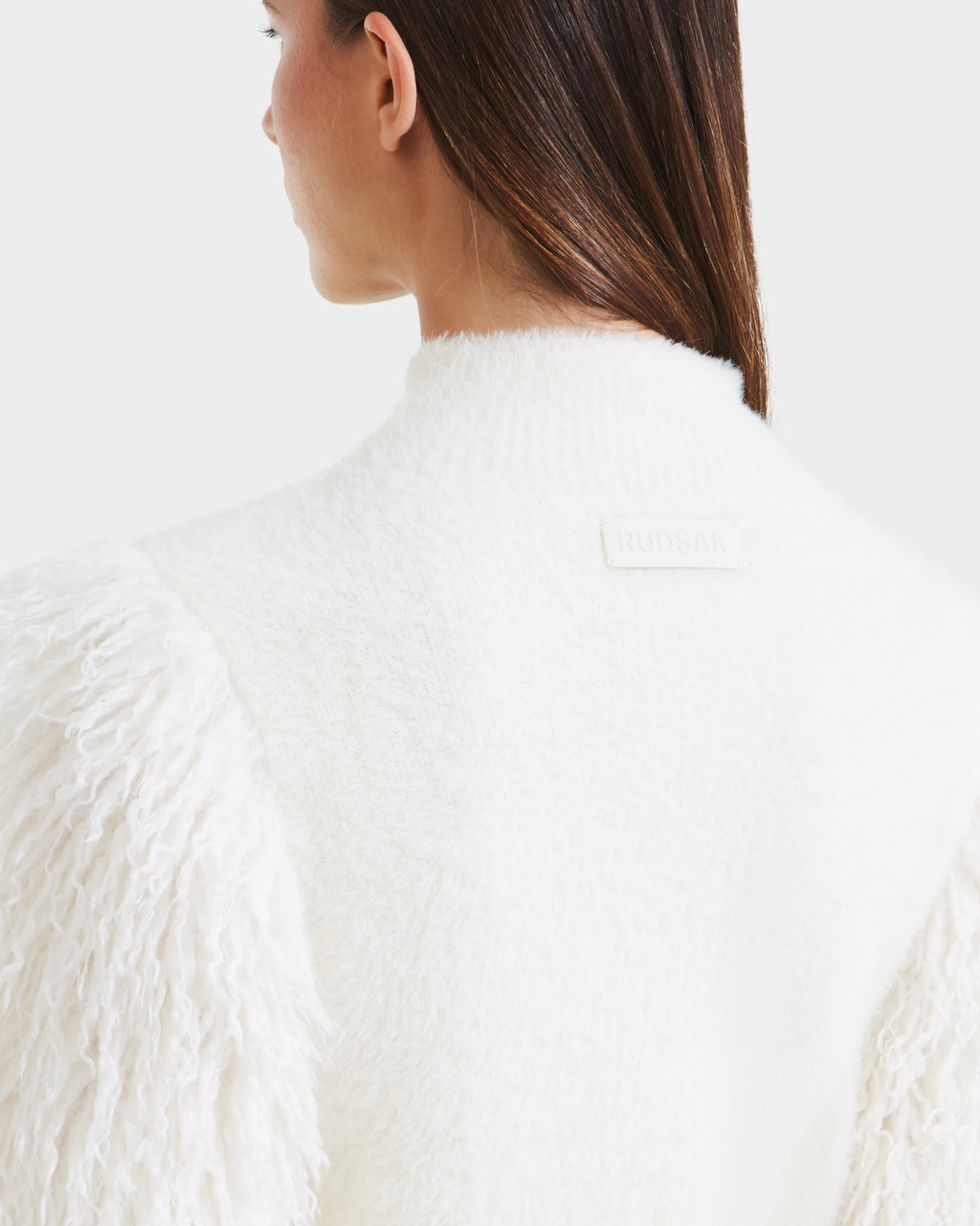 A woman with straight brown hair is seen from behind wearing the Rudsak NOEL - 8525571 Vanilla textured white jacket with faux fur sleeves, featuring the Rudsak label at the collar—ideal for chic winter looks against a white background.