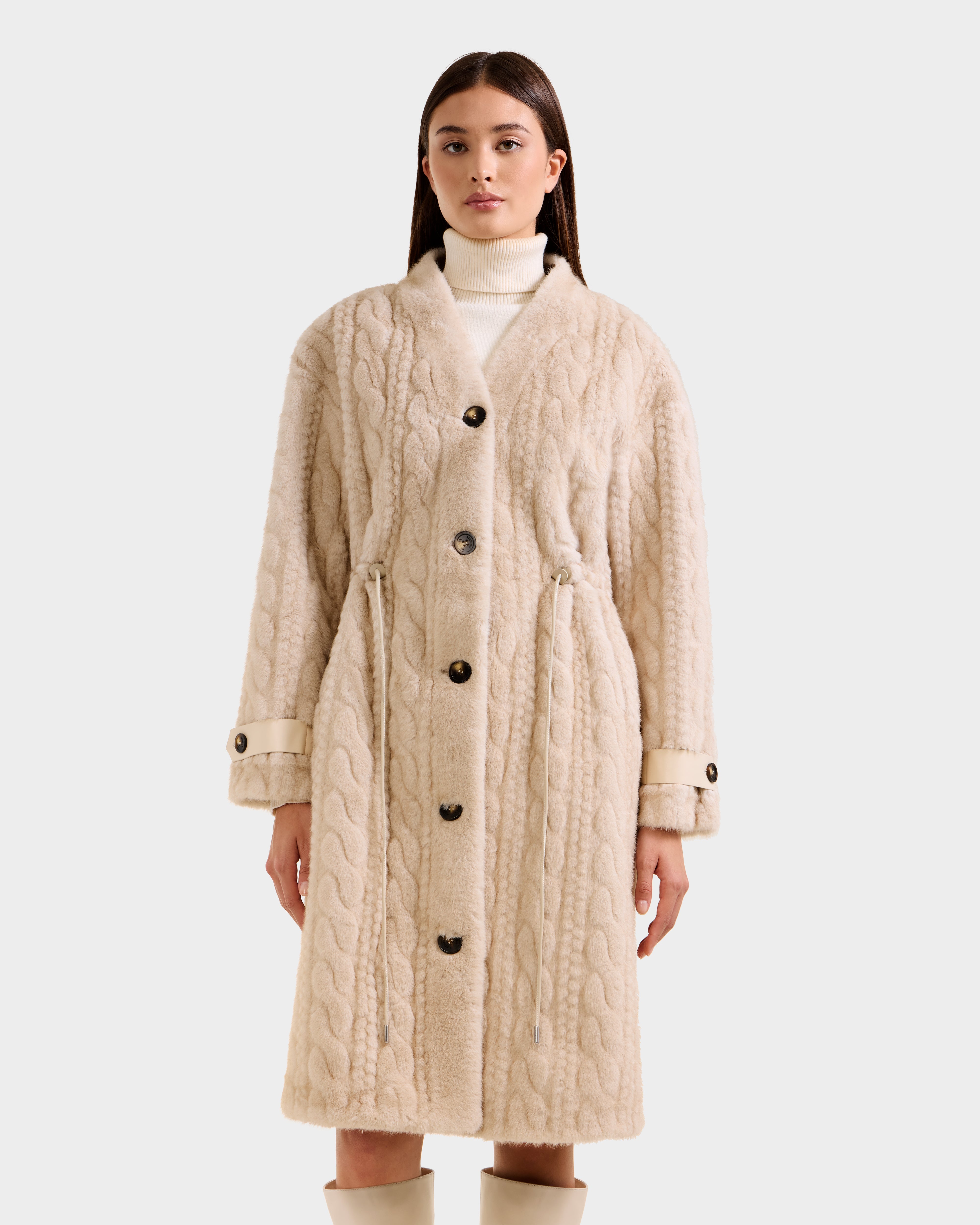 A woman models the Rudsak ORIANA - 8125545 Vanilla cream cable knit coat with large buttons, paired with a white turtleneck and beige knee-high boots against a plain light background.
