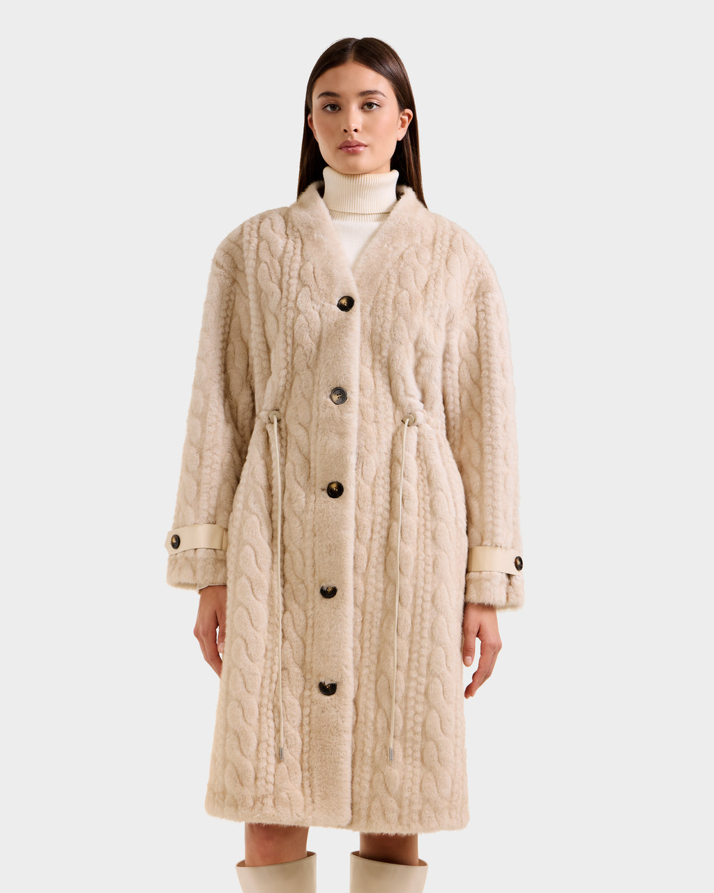 A woman models the Rudsak ORIANA - 8125545 Vanilla cream cable knit coat with large buttons, paired with a white turtleneck and beige knee-high boots against a plain light background.