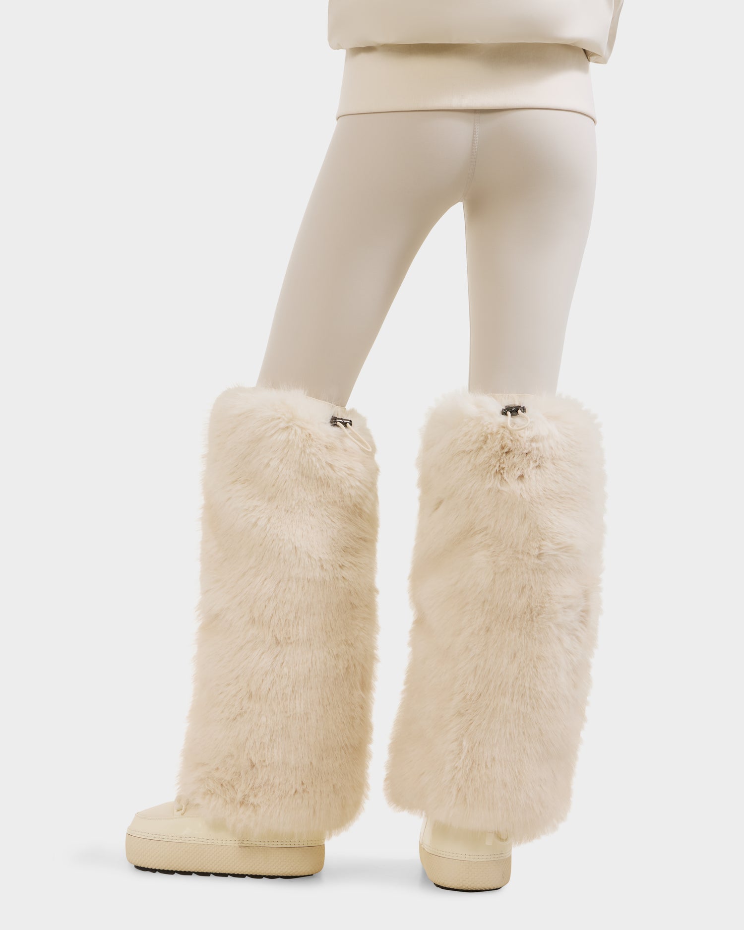 A person from behind wears PAIGE - 8425534 Vanilla leggings by Rudsak, paired with matching shoes and plush faux fur leg warmers—an essential women’s winter accessory—showcasing après-ski chic on a clean white background.