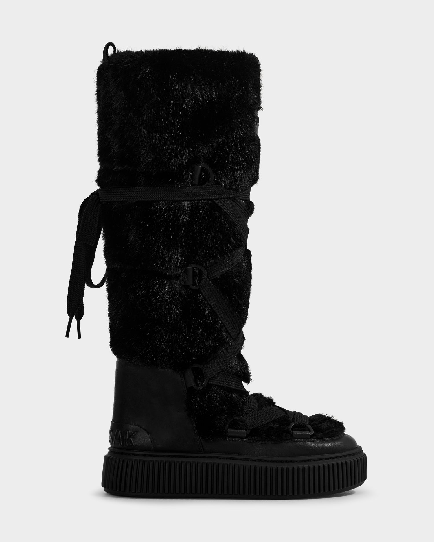 The Rudsak PALERMO C - 8225546 Black is a tall women's faux fur winter boot with a thick textured sole and crisscross lace-up front, shown in profile against a plain white background.