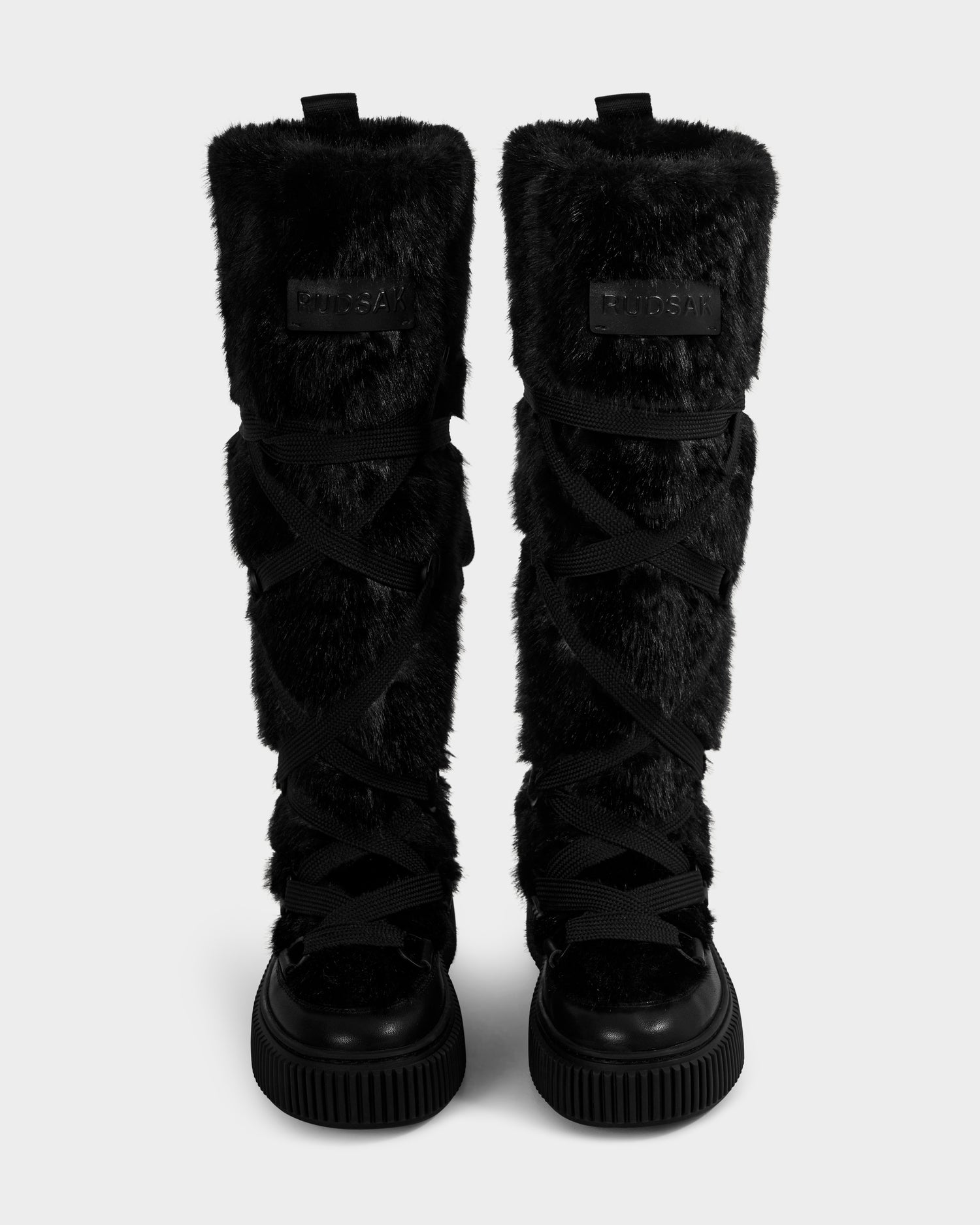 The PALERMO C - 8225546 Black women's winter boots by Rudsak feature tall black faux fur, thick crisscross laces, and chunky rubber soles, shown upright side by side on a plain light gray background.