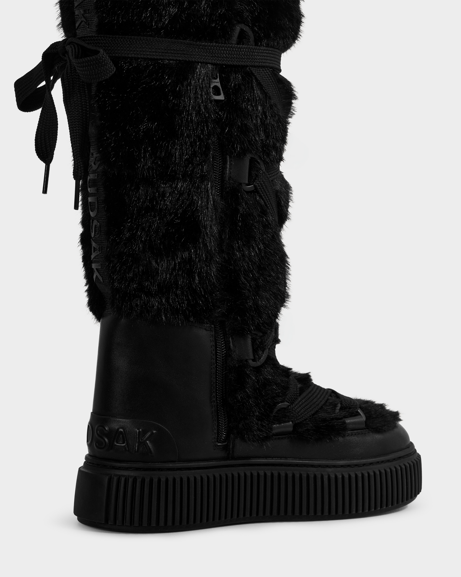 The Rudsak PALERMO C - 8225546 Black is a women's knee-high faux fur winter boot with a thick rubber sole, lace-up front, side zipper, and signature branding—ideal for stylish après-ski wear.