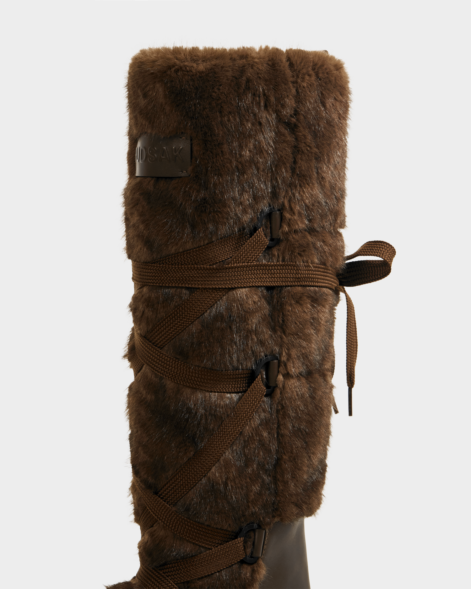 A close-up of the Rudsak PALERMO C - 8225546 Mocha women’s faux fur winter boot, featuring decorative brown side laces, a cozy cable knit accent, shown against a plain light background.