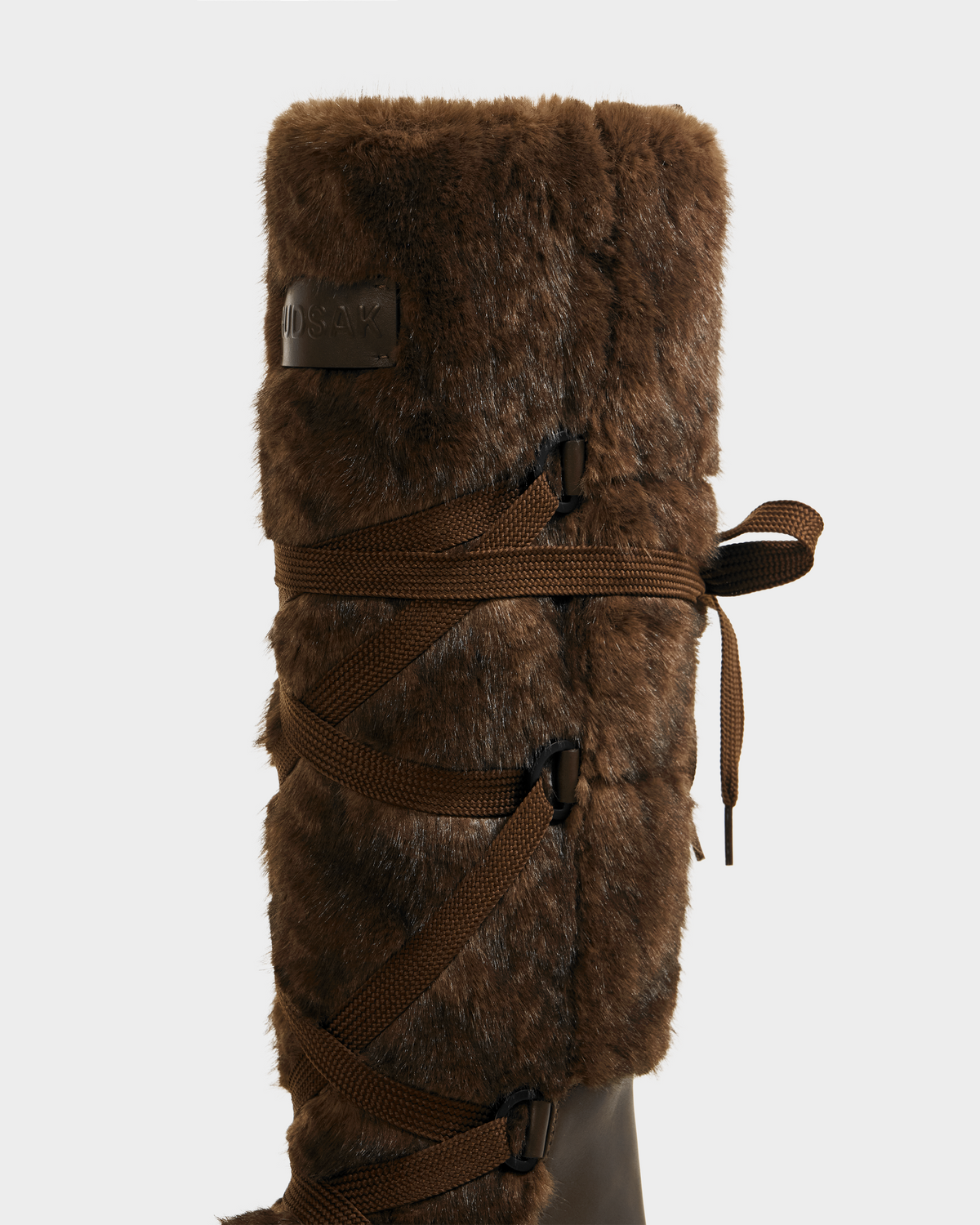 A close-up of the Rudsak PALERMO C - 8225546 Mocha women’s faux fur winter boot, featuring decorative brown side laces, a cozy cable knit accent, shown against a plain light background.