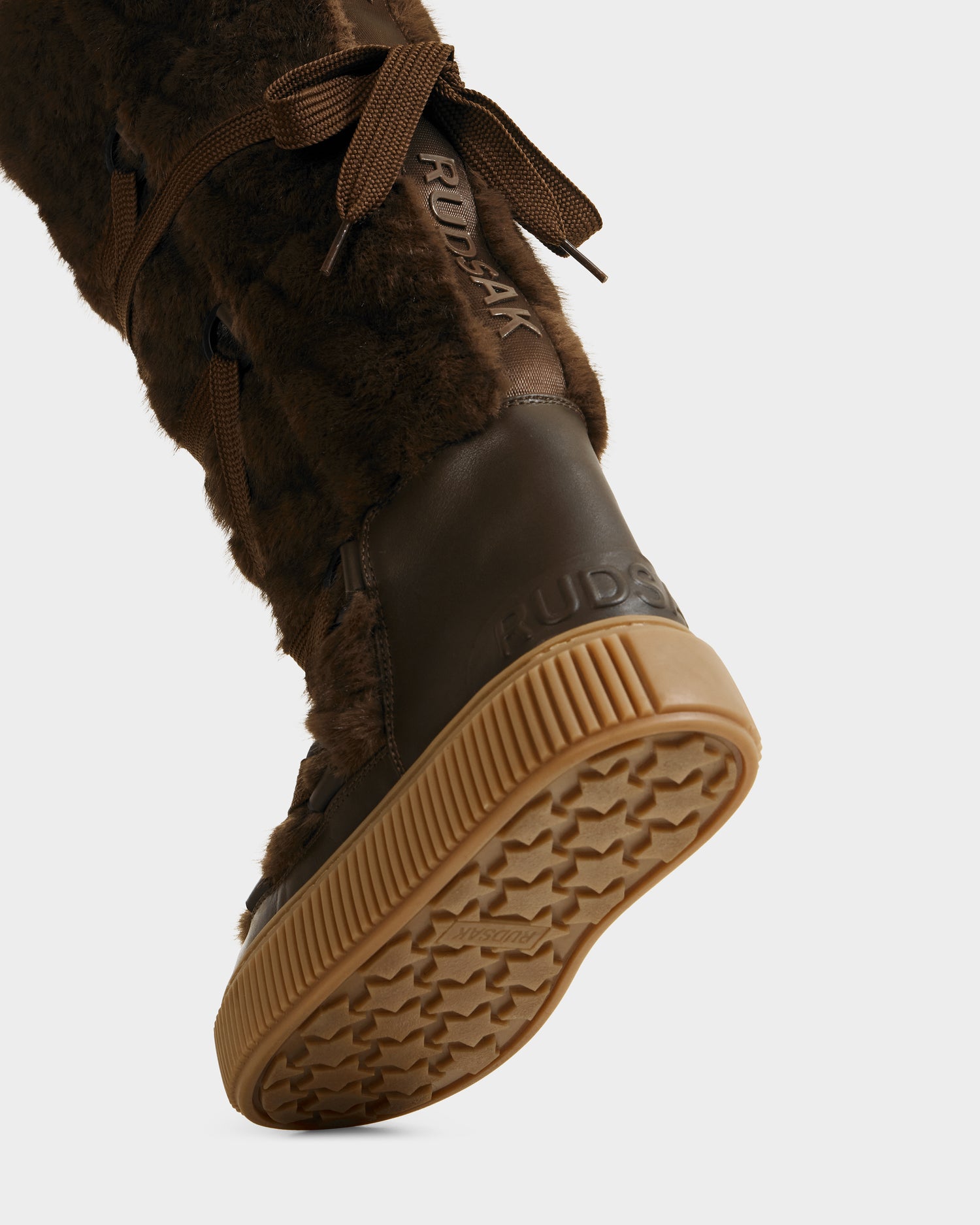 Close-up of the Rudsak PALERMO C - 8225546 Mocha women's faux fur winter boot featuring fur details, a rubber sole with tread pattern, and visible Rudsak branding on the heel and upper of this stylish footwear.
