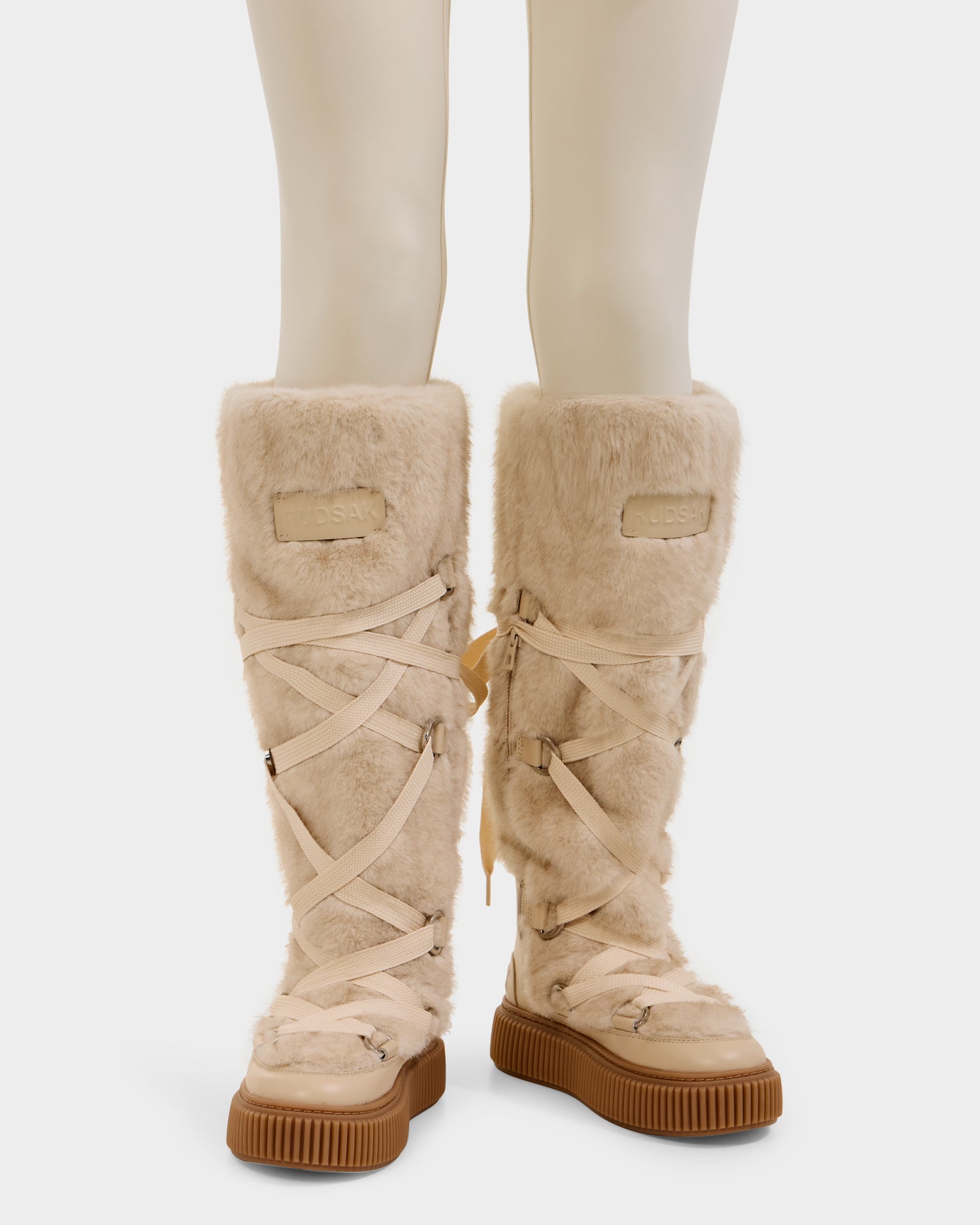 Front view of Rudsak's PALERMO C - 8225546 Vanilla women's faux fur winter boots in beige, with crisscrossed laces and thick brown soles, shown on a mannequin—perfect for stylish après-ski looks.