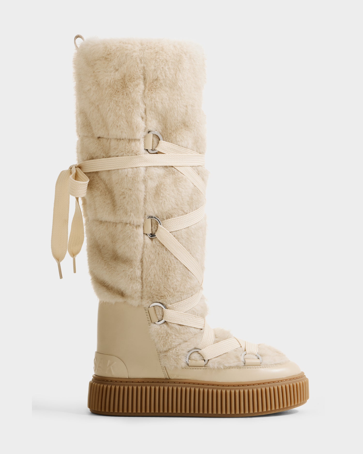 The Rudsak PALERMO C - 8225546 Vanilla is a tall beige women’s faux fur winter boot with cream laces, metal loops, a ribbed light brown rubber sole—perfect for stylish winter wear.