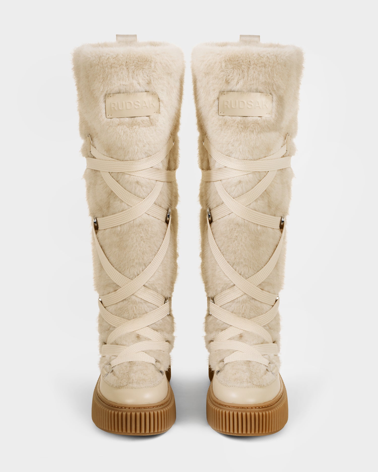 A pair of Rudsak PALERMO C - 8225546 Vanilla knee-high women’s faux fur winter boots with cream uppers, crisscrossing beige laces, tan rubber soles, and a front brand patch are shown facing forward.