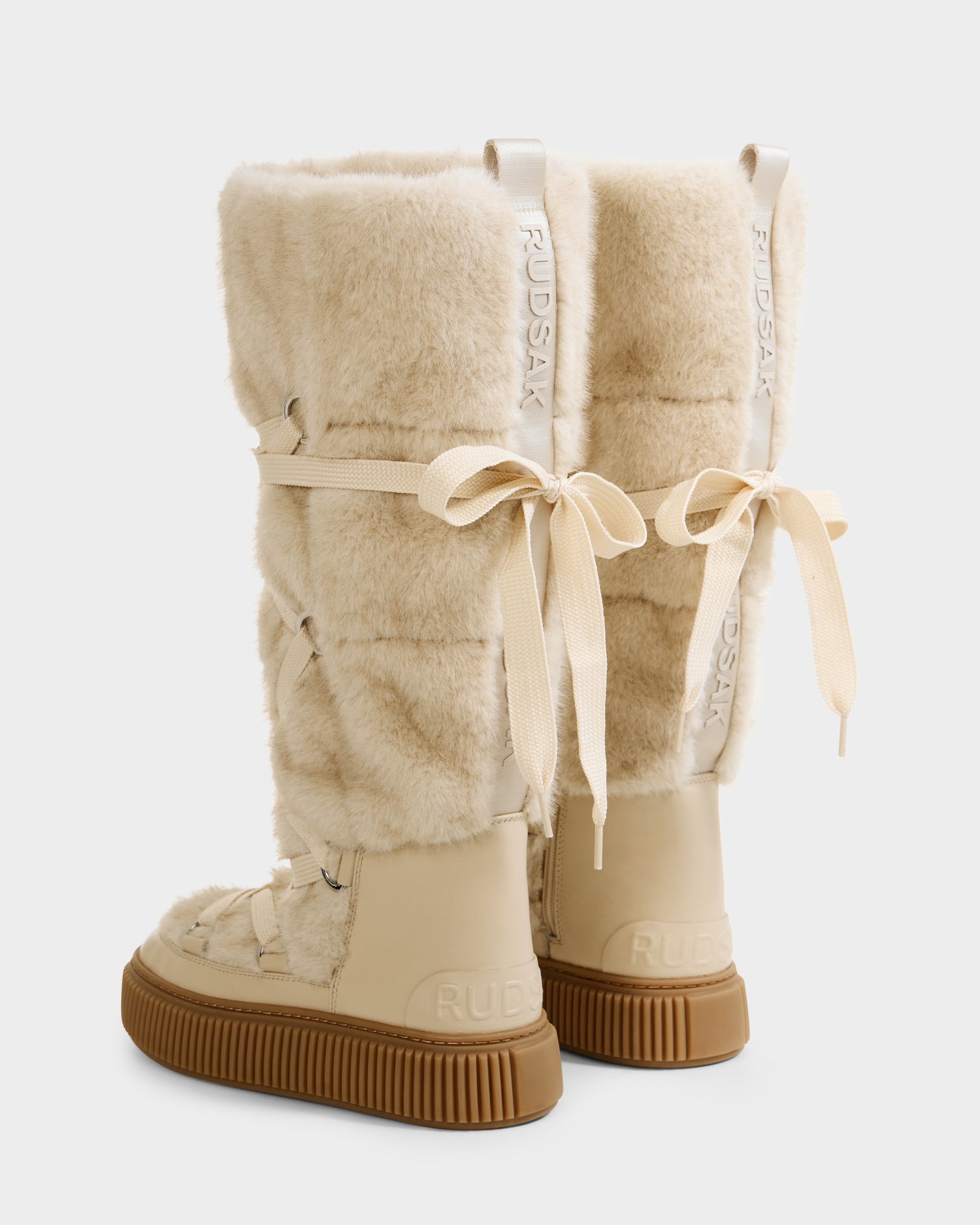 The Rudsak PALERMO C - 8225546 Vanilla are tall beige women's faux fur winter boots with rubber soles, lace-up cream ribbon backs, branded pull tabs, and a plush après-ski look.