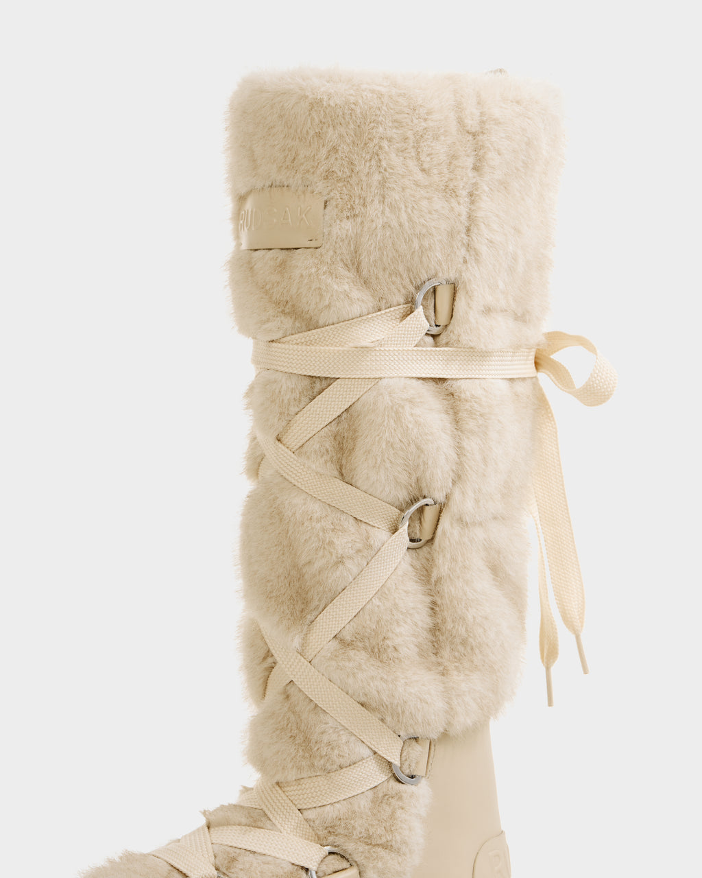 A close-up of the Rudsak PALERMO C - 8225546 Vanilla knee-high women’s faux fur winter boot with a light beige, fluffy texture and cream crisscross side laces, perfect for winter, set against a plain white background.