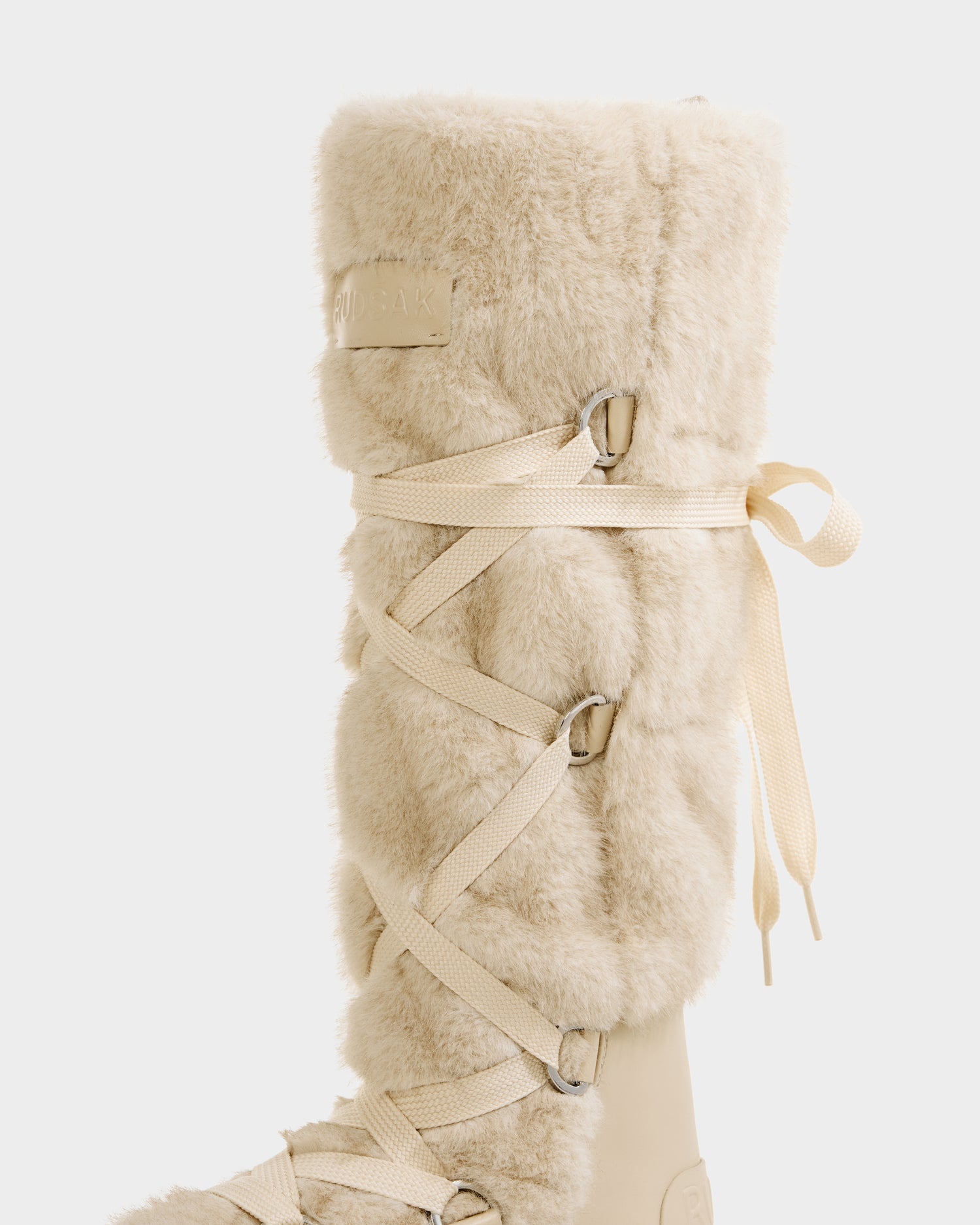A close-up of the Rudsak PALERMO C - 8225546 Vanilla knee-high women’s faux fur winter boot with a light beige, fluffy texture and cream crisscross side laces, perfect for winter, set against a plain white background.