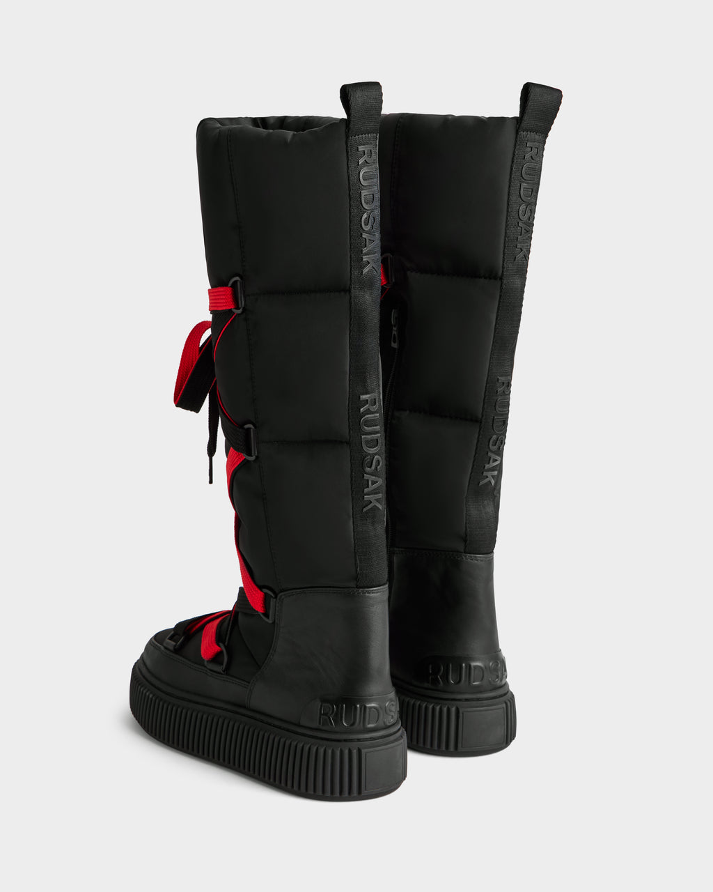 Two tall black PALERMO - 8225030 women’s winter boots by Rudsak feature thick soles, a water-resistant quilted design, red back laces, and RUDSAK embossed on the heel and vertically along the back.