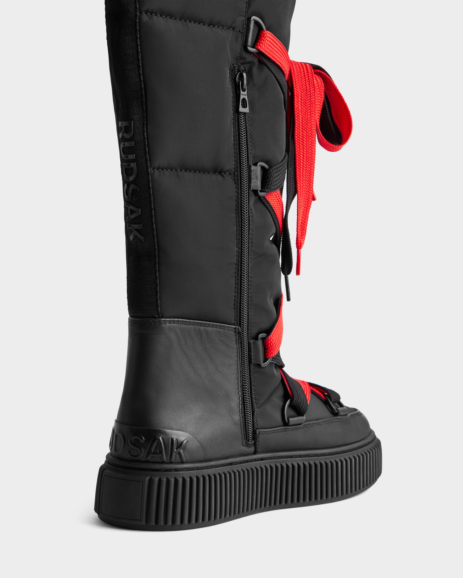 The PALERMO - 8225030 Black by Rudsak is a tall black women’s winter boot with thick red laces, side zipper, ridged platform sole, water-resistant insulation, and RUDSAK embossed near the ankle and heel.
