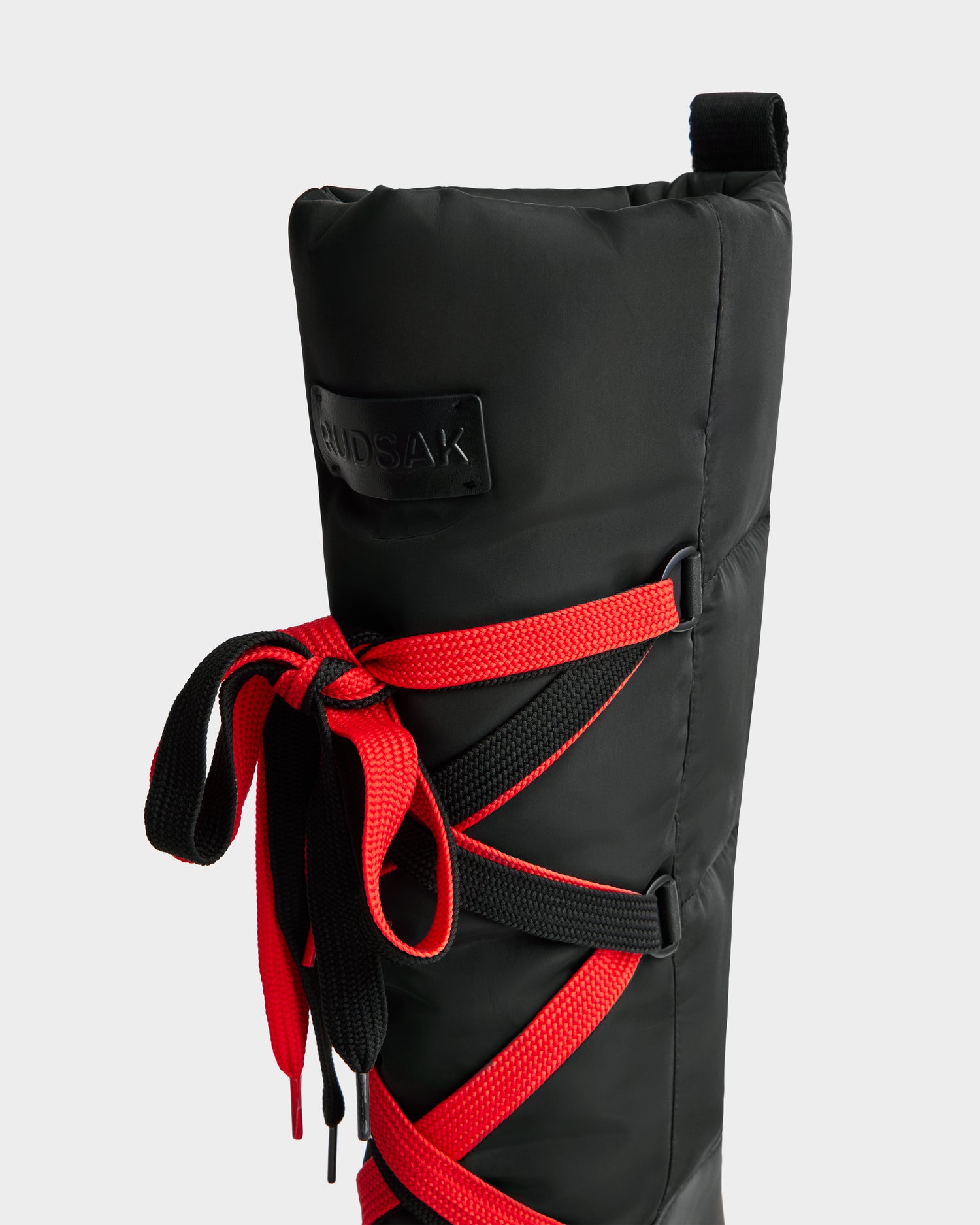 Close-up of the Rudsak PALERMO - 8225030 women’s winter boot in black, featuring red crisscross laces, a fabric pull tab at the top, and a visible brand patch.