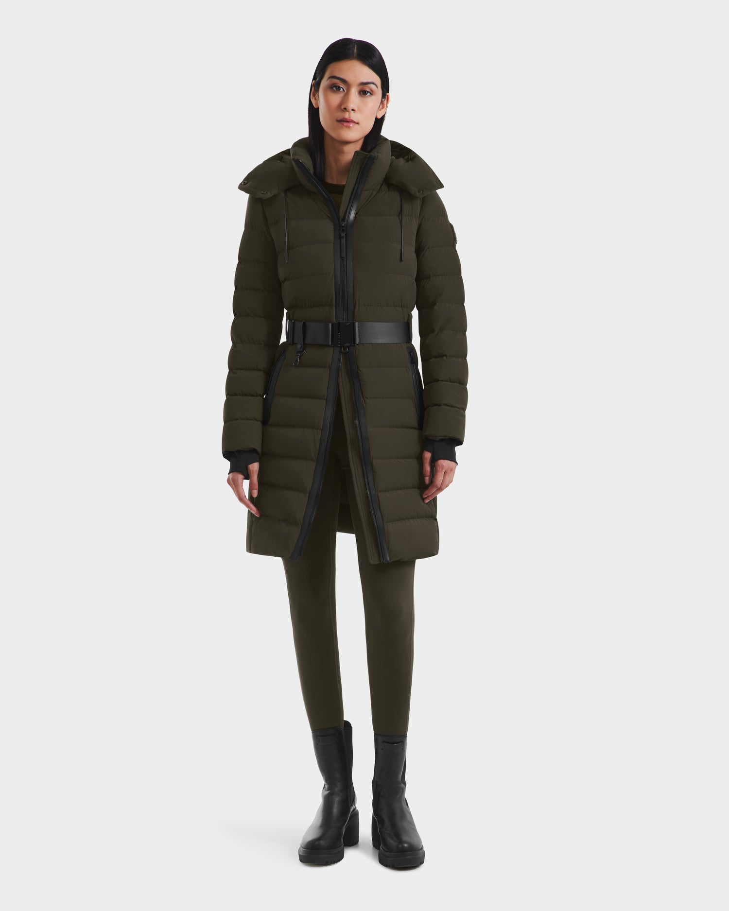 A woman faces forward in a Rudsak PELIN M - 8124814 dark olive womens down puffer coat with a belt, matching green pants, and black ankle boots against a plain white background.