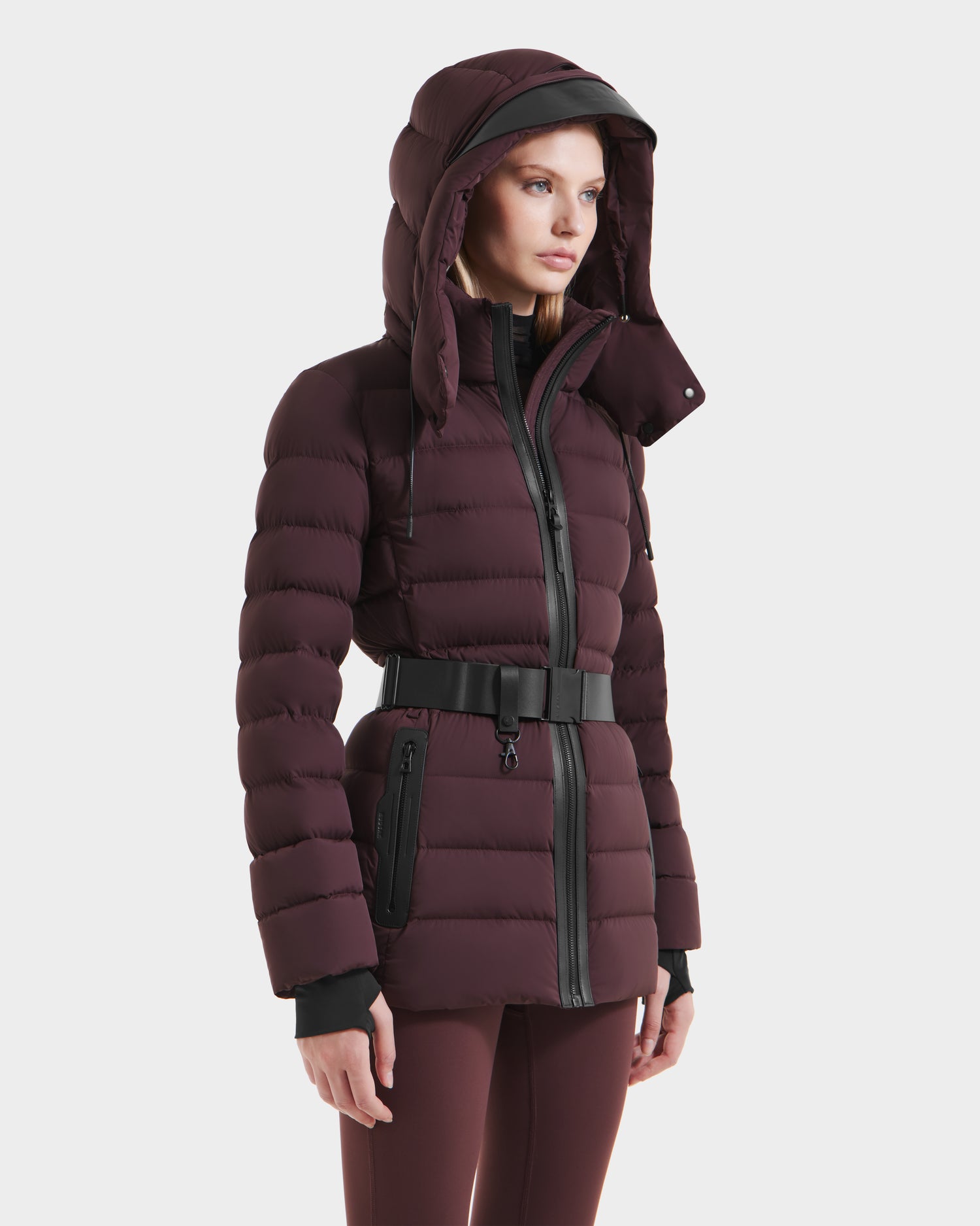 A woman wears the Rudsak PELIN S - 8124813 Bordeaux down puffer jacket, featuring a hood and black zipper details, standing against a plain white background.