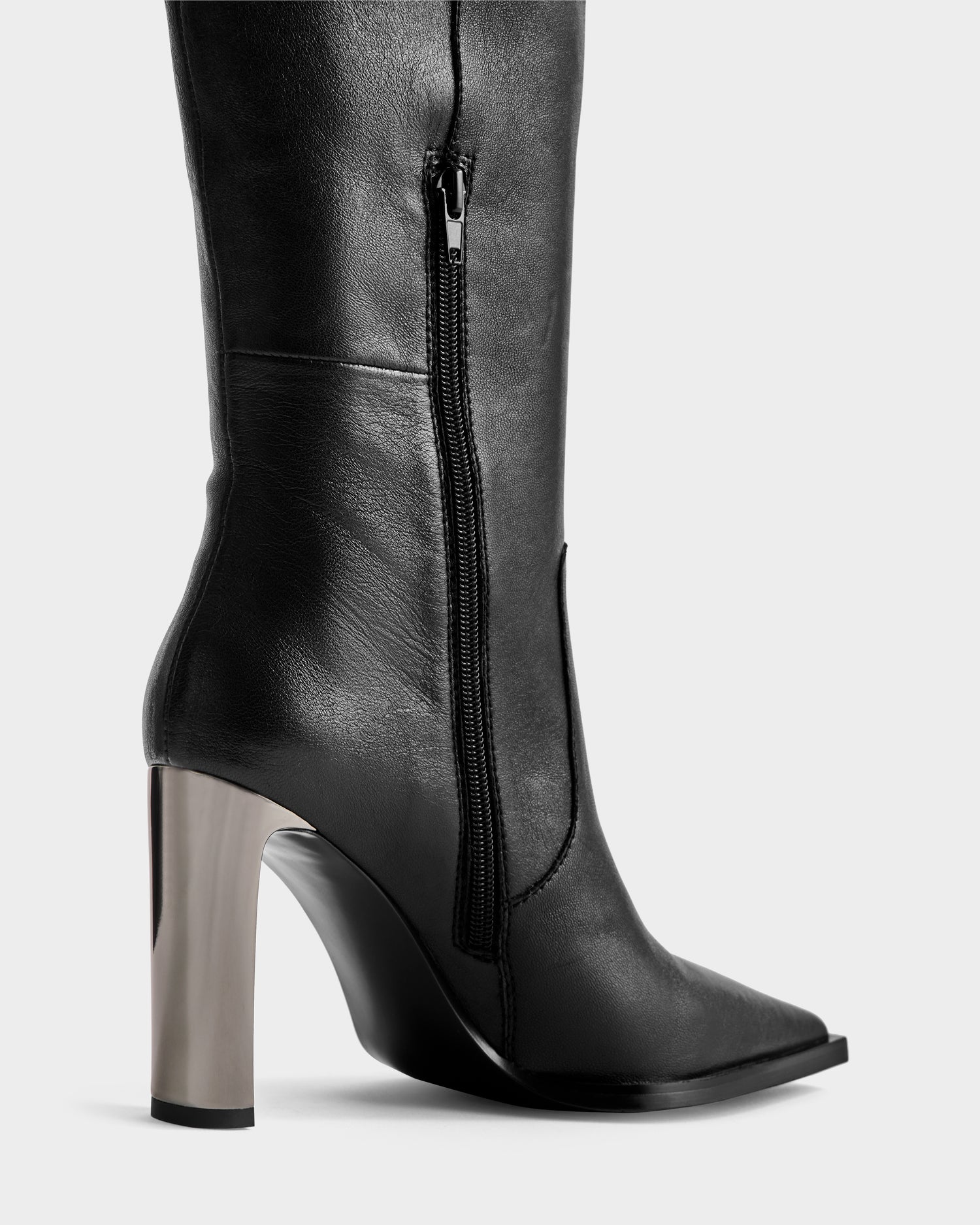 Side view of Rudsak’s PERNA - 8225555 Black tall leather boot with a pointed toe, visible zipper, and high chunky metallic heel—stylish winter statement boots set against a plain light background.