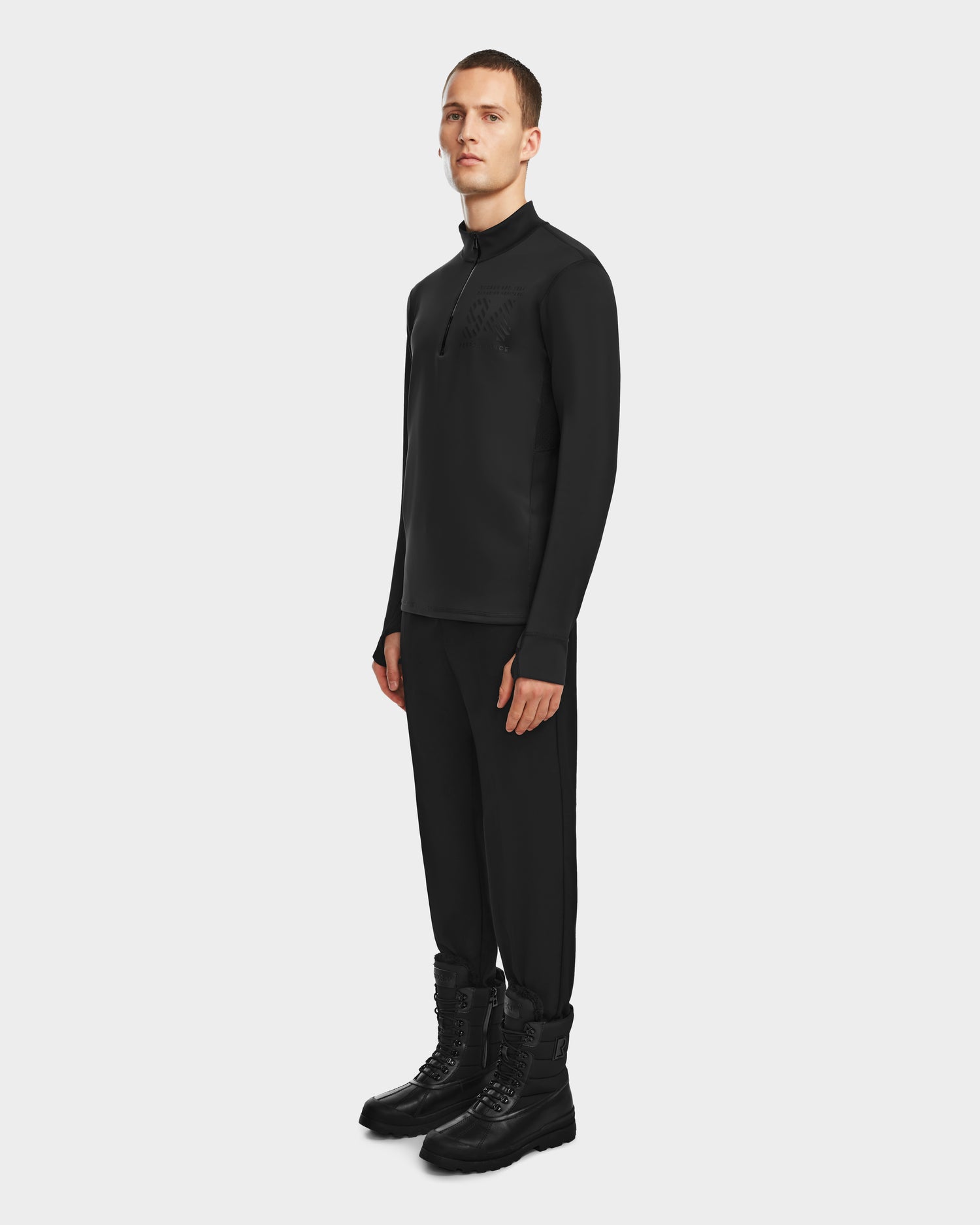 A person stands against a plain background wearing Rudsak’s RALI - 6524522 Black men’s active top and pants with black lace-up boots—ideal for layering or winter sports—and looks forward with a neutral expression.