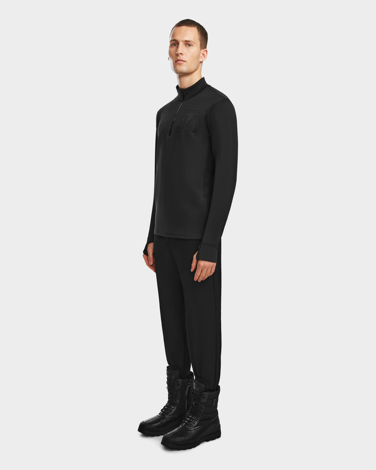 A person stands against a plain background wearing Rudsak’s RALI - 6524522 Black men’s active top and pants with black lace-up boots—ideal for layering or winter sports—and looks forward with a neutral expression.