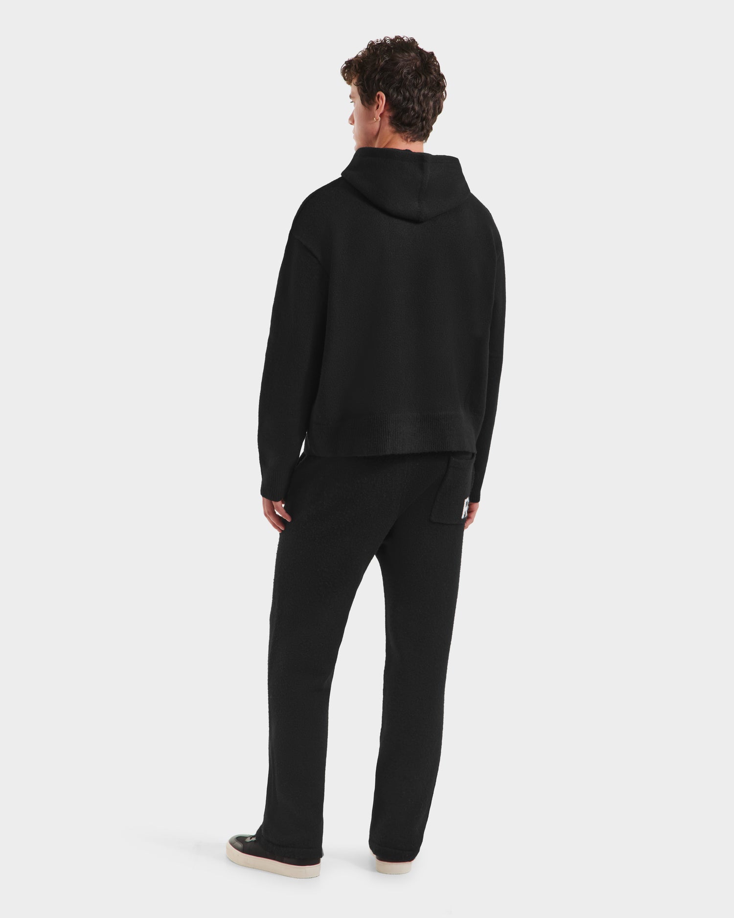 A person with short curly hair is facing away, wearing the RAPHAEL - 6525643 Black hoodie and pants by Rudsak, paired with light sneakers, on a plain white background.
