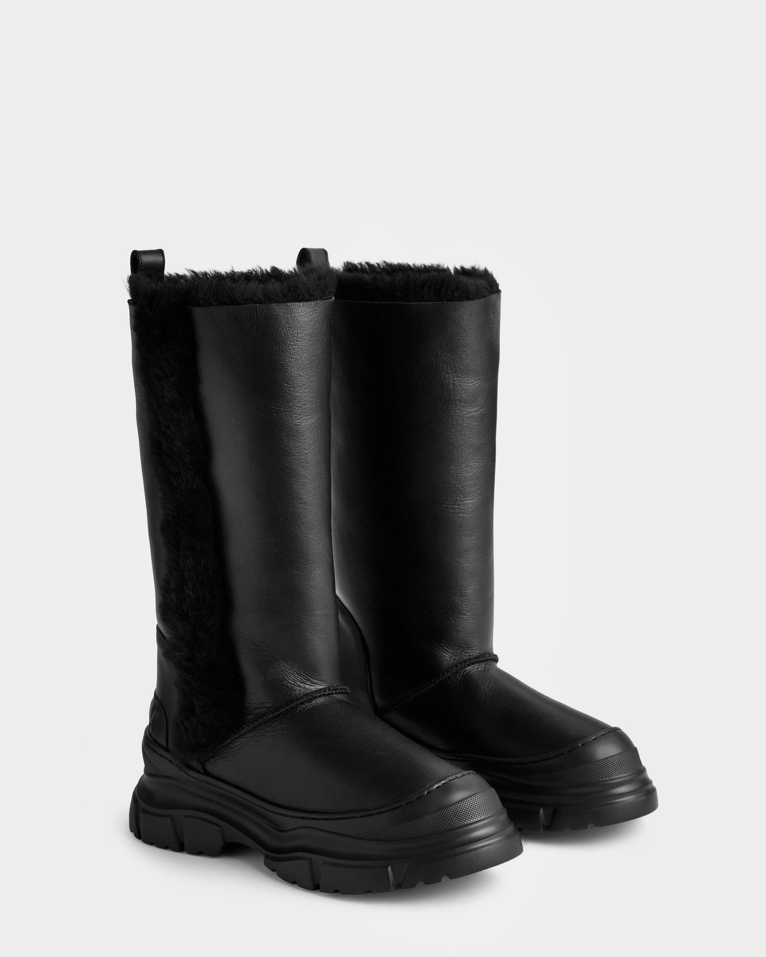 The RAVENNA - 8225031 Black winter boots by Rudsak are tall women’s boots with thick chunky soles, faux fur lining at the sides and top, a smooth leather-like finish, and convenient pull tabs.