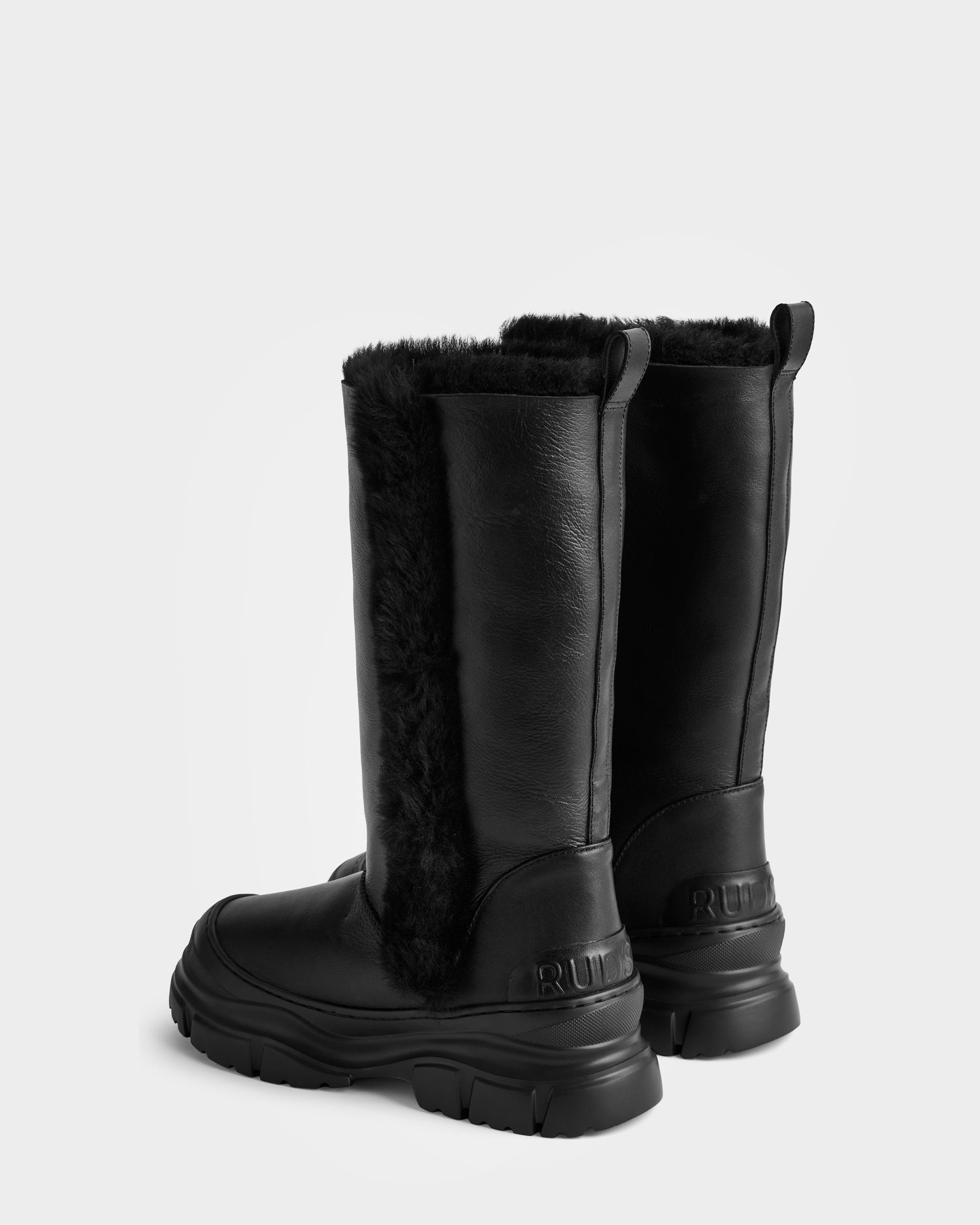 A pair of tall black women’s winter boots—RAVENNA - 8225031 Black by Rudsak—feature thick soles, faux fur lining, and back pull tabs, styled on a plain white background for a cozy winter look.