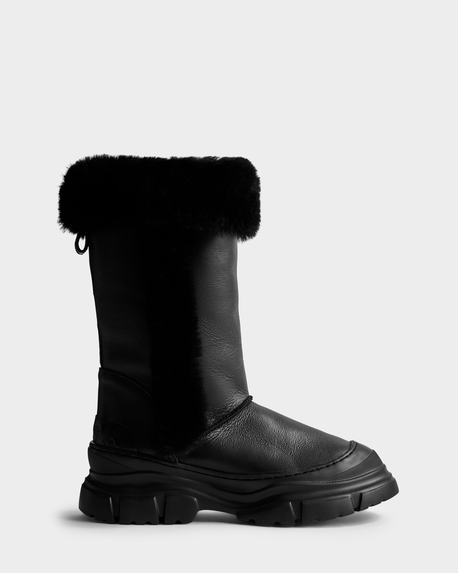 The Rudsak RAVENNA - 8225031 Black is a women’s high winter boot with a chunky sole, thick textured tread, soft furry black cuff, cozy shearling lining, and sleek leather-like exterior on a plain light gray background.