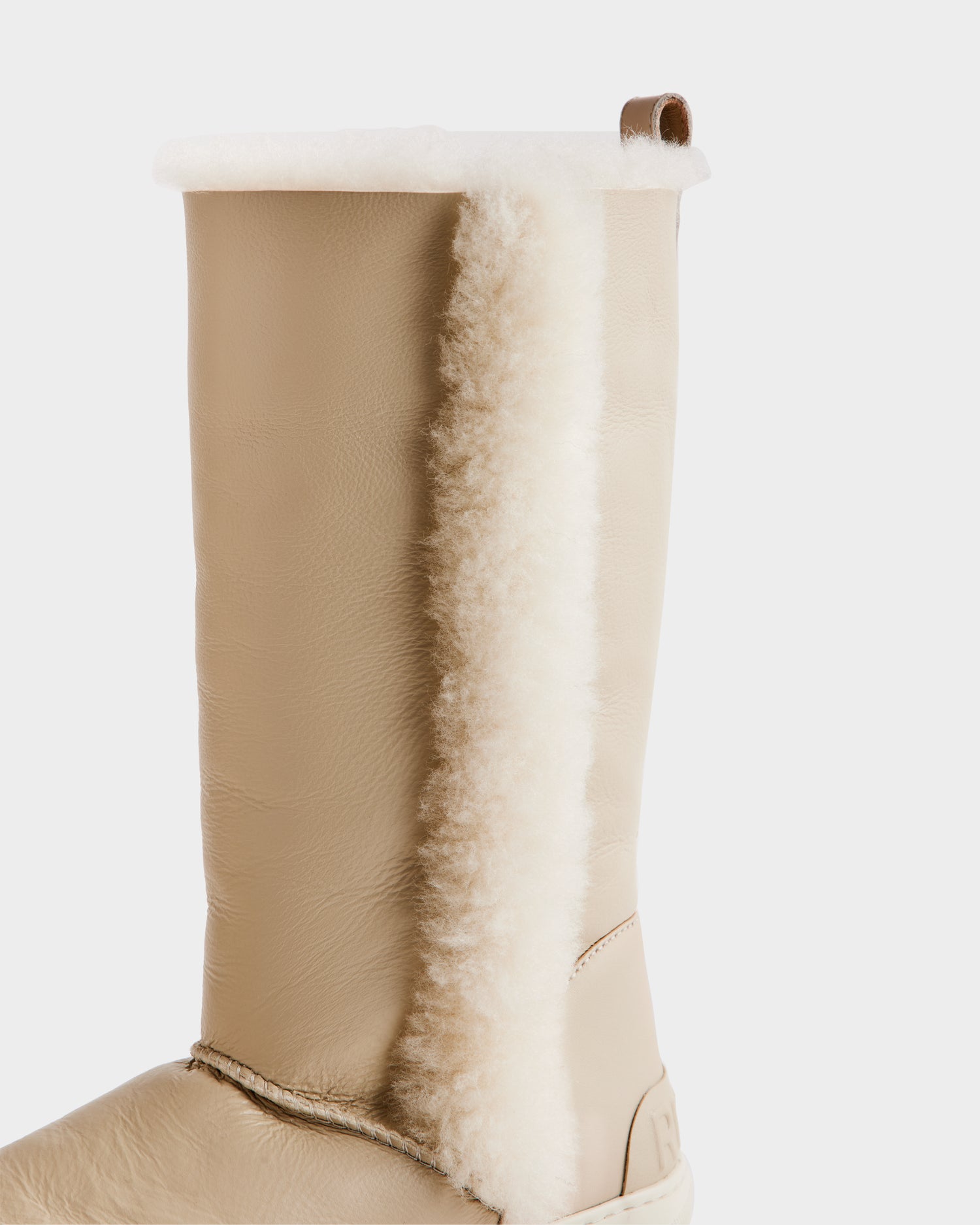 A close-up of the Rudsak RAVENNA - 8225031 Vanilla women’s winter boot, featuring a beige leather exterior and a vertical strip of white shearling lining on the side, set against a plain white background.
