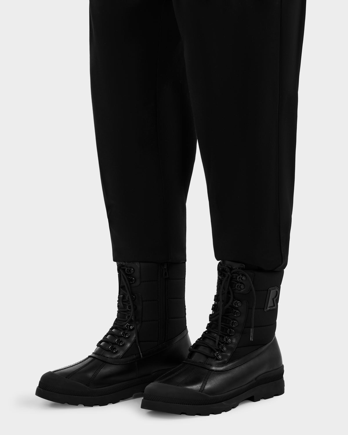Rudsak REAGAN - 6225046 Black leather boots with a quilted upper and a rubberized lower section, worn with black trousers.