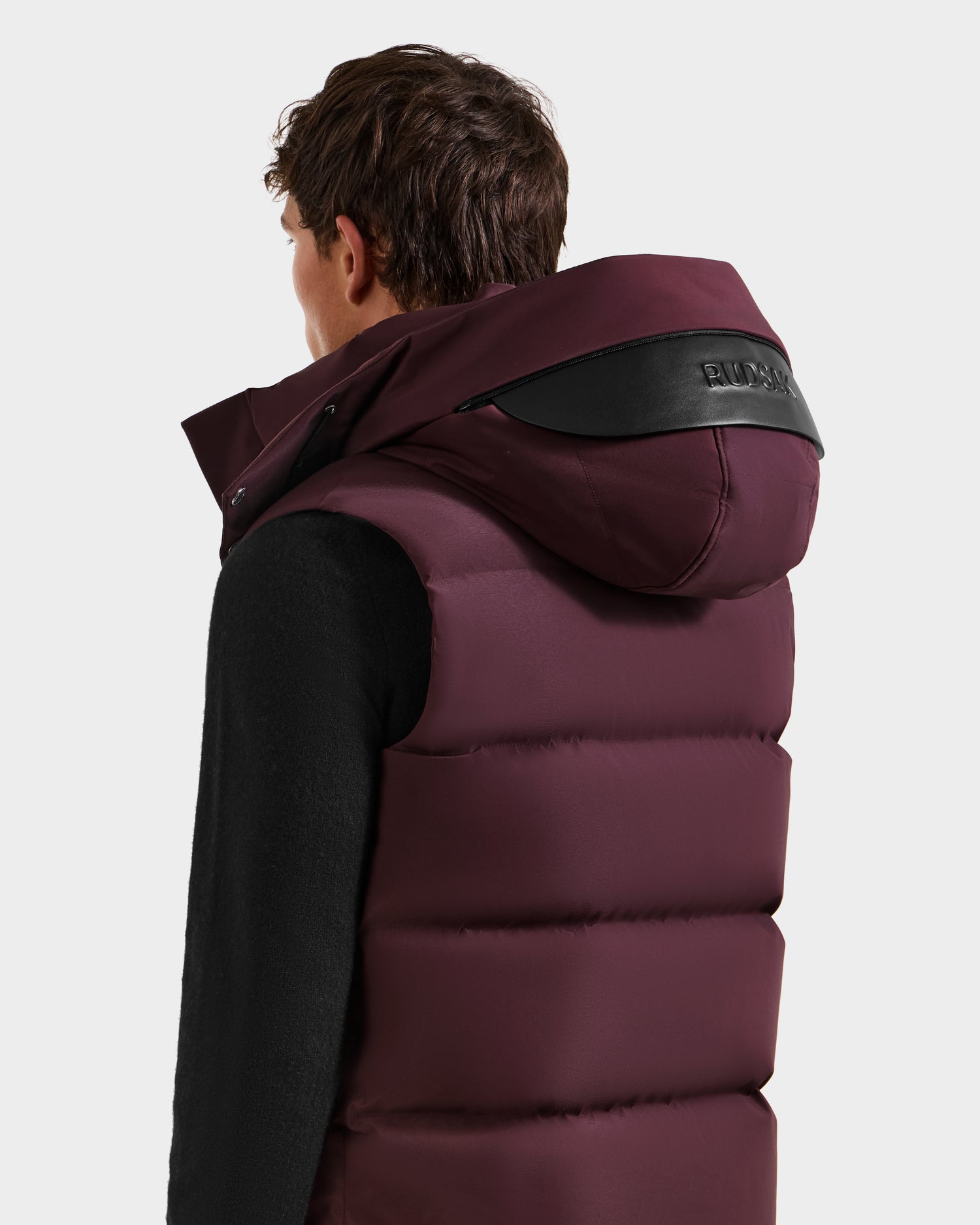 A person faces away in a Rudsak REN H - 6125688 Bordeaux men’s quilted down puffer vest with removable hood and black accents, set against a plain white background—an ideal cold-weather essential.