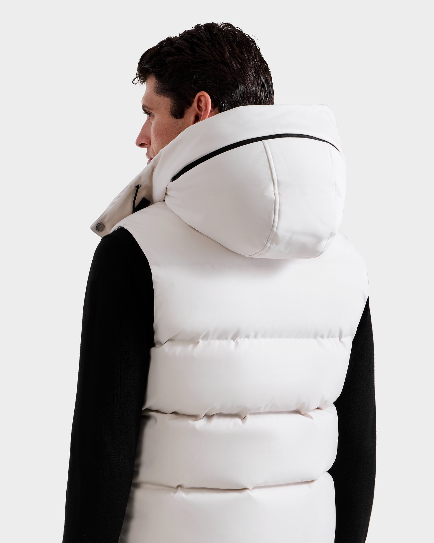 A person with short dark hair, in a black long-sleeve shirt and the Rudsak REN H - 6125688 Vanilla men’s quilted down puffer vest with removable hood, is shown from the back against a plain light background—a cold-weather essential.