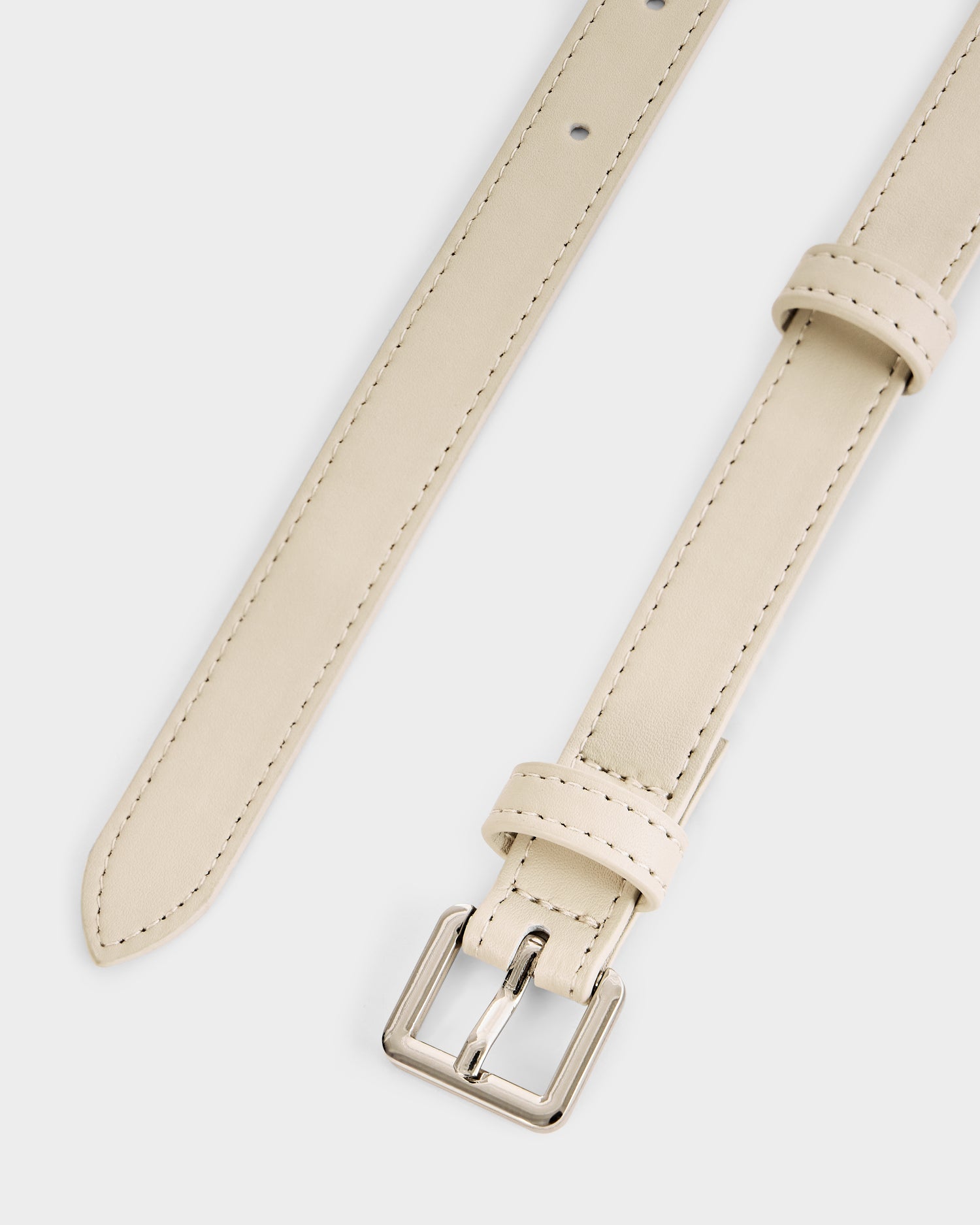 A close-up of the RENA - 8425039 Vanilla wrap belt by Rudsak: a thin, light beige women’s leather belt with a silver buckle and matching beige stitching, shown on a white background. Perfect for accentuating your waist.