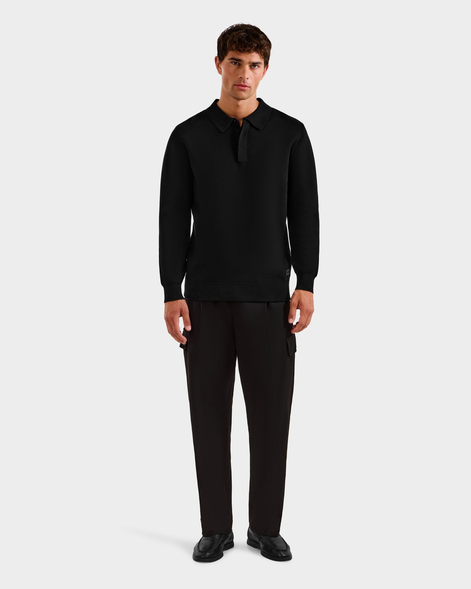 A man faces forward against a white background, wearing the RICHARD - 6524529 Black men's knit polo sweater by Rudsak, paired with dark dress pants and black shoes.