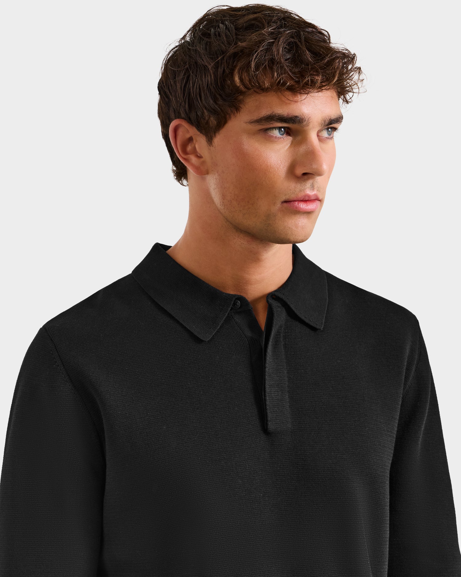 A young man with short, wavy brown hair wears the Rudsak RICHARD - 6524529 Black men's knit polo sweater. He looks slightly to his left, set against a plain, light gray background.