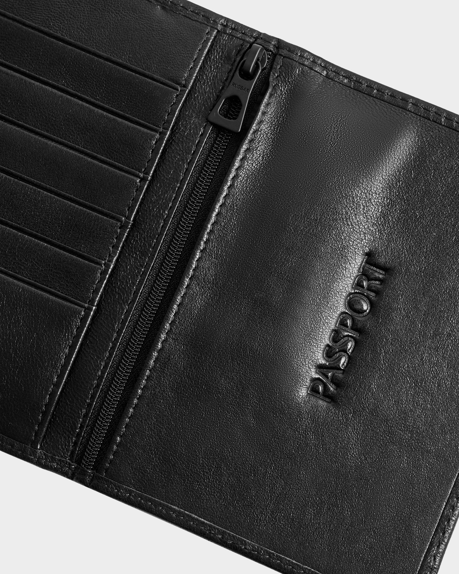 A close-up of the ROBIN - 9425562 Black by Rudsak, a sleek unisex leather passport holder with card slots, zippered pocket, and PASSPORT embossed on the right side.