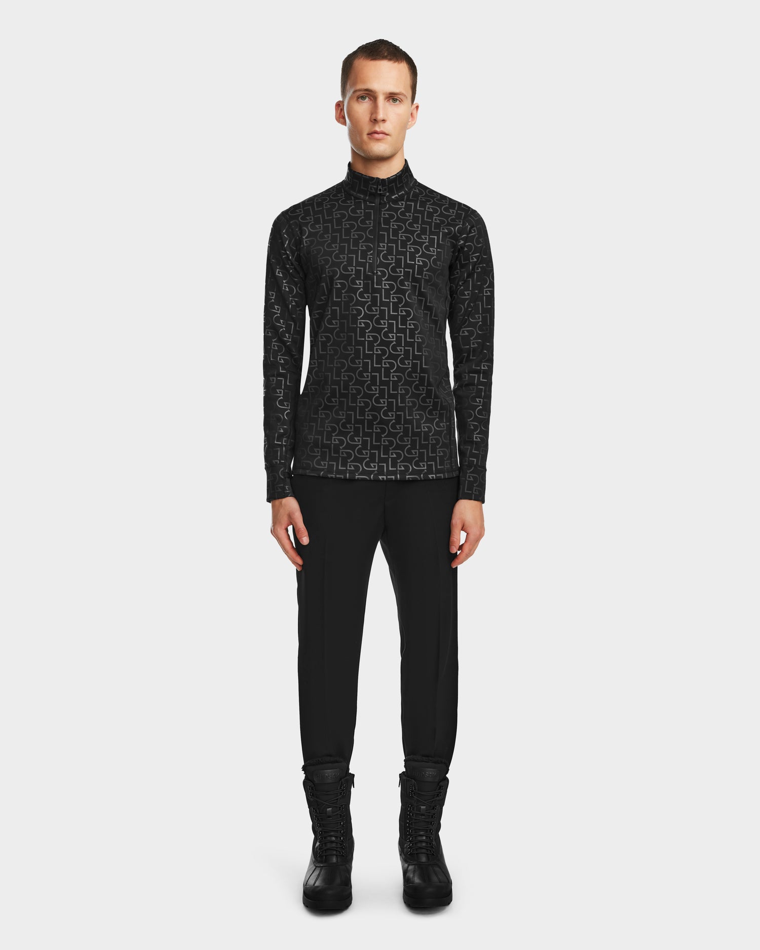A man faces forward in the Rudsak ROMEO - 6524525 Black mock neck zip-up, black pants, and lace-up boots—showcasing sleek cold-weather activewear against a plain white background.