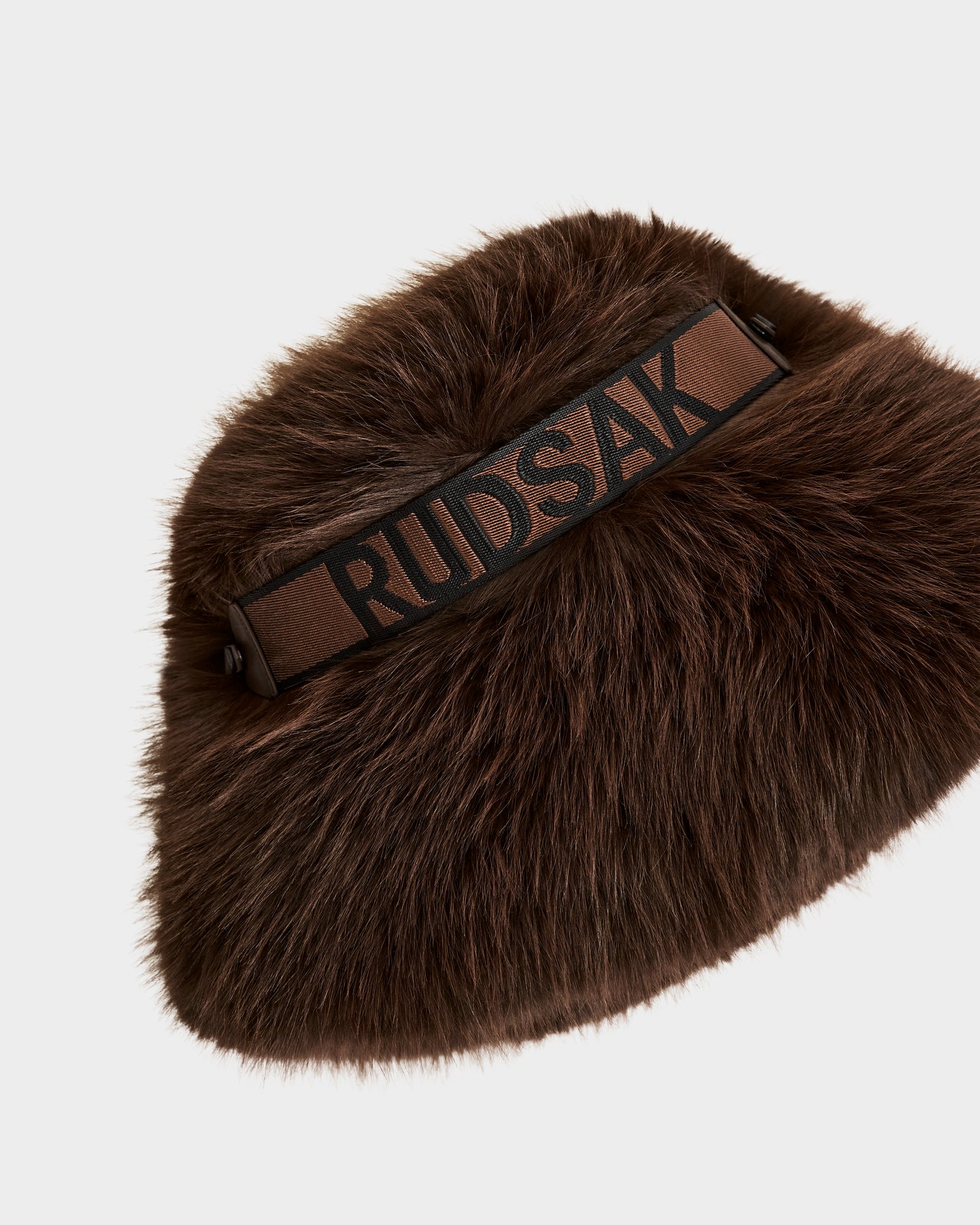 The ROMINA - 8425545 Espresso by Rudsak is a brown faux fur bag with a black and brown strap, featuring the Rudsak name in bold black letters. It's a cozy-luxe accessory, ideal to pair with your favorite women’s winter hat.