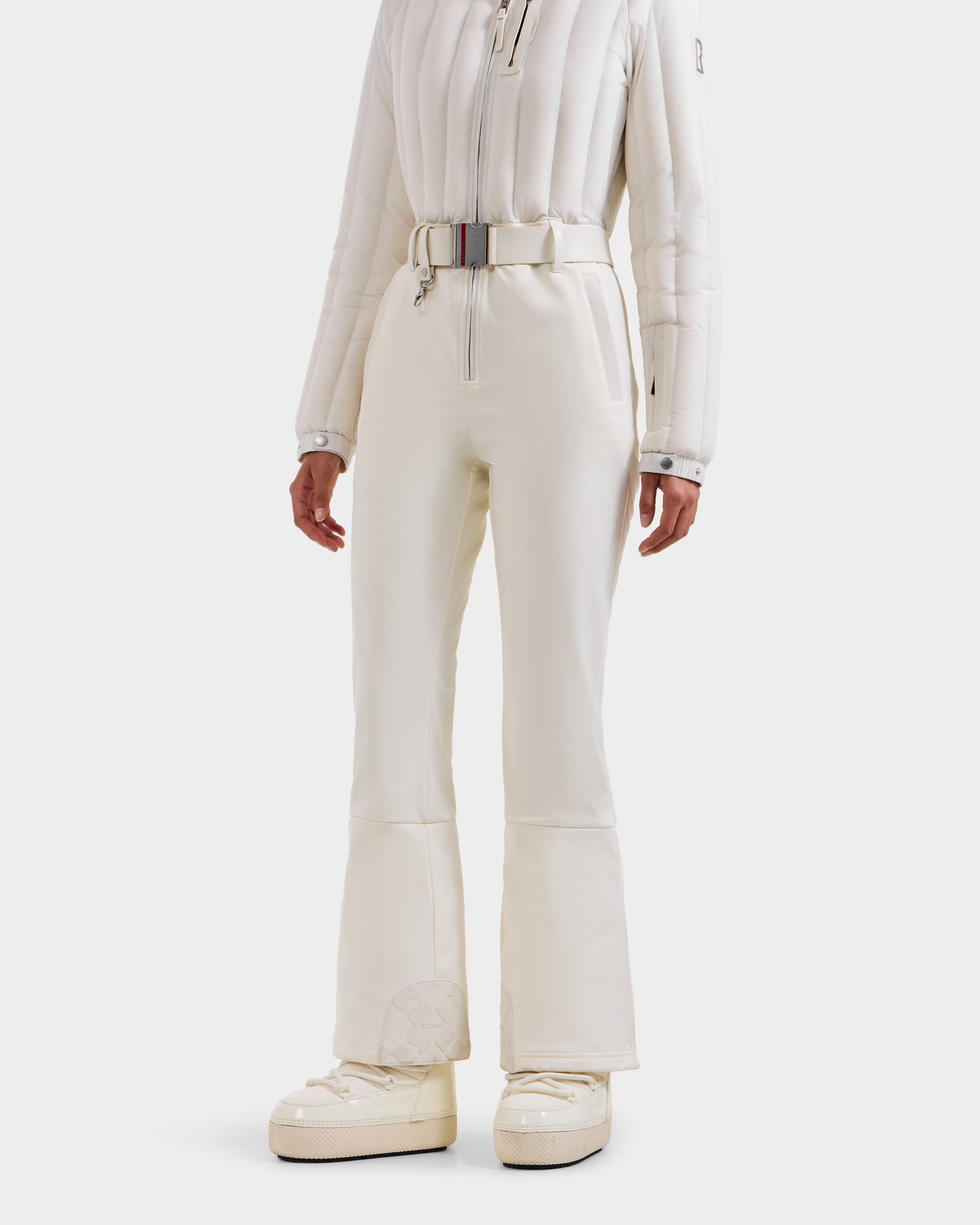 A person wears the Rudsak SAGE - 8124782 Iceland white quilted women’s ski suit with high-waisted belted pants and ivory platform snow boots, standing against a plain white background—ideal for technical performance on the slopes.