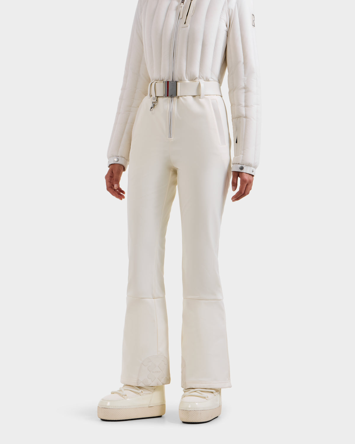 A person wears the Rudsak SAGE - 8124782 Iceland white quilted women’s ski suit with high-waisted belted pants and ivory platform snow boots, standing against a plain white background—ideal for technical performance on the slopes.