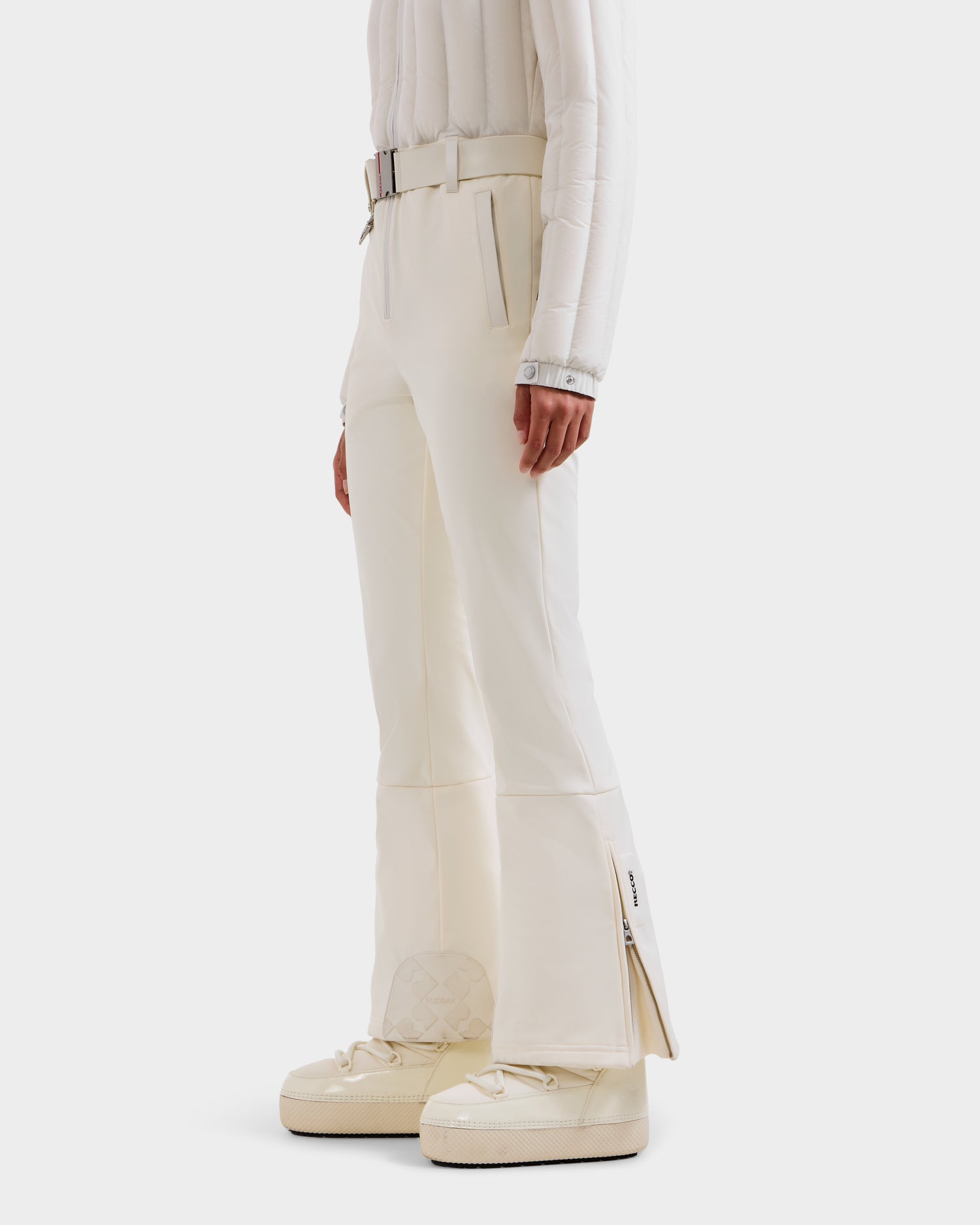 A person models the Rudsak SAGE - 8124782 Iceland: white flared pants with ankle zippers and a matching belted top, styled with white sneakers, against a plain white background.