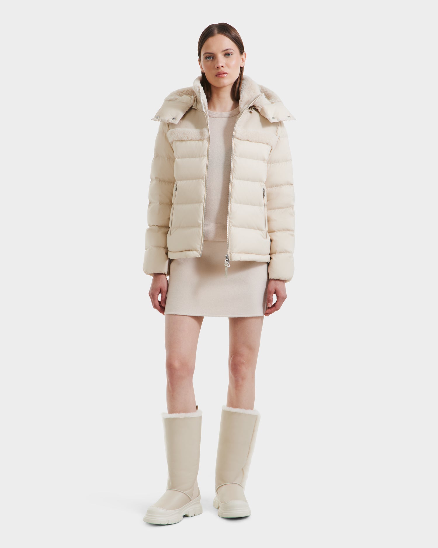 A woman faces forward in a modern look, wearing the Rudsak SANDRA - 8125612 Vanilla women’s shearling puffer jacket with a matching short dress and knee-high boots. She has straight brown hair and a neutral expression against a white background.
