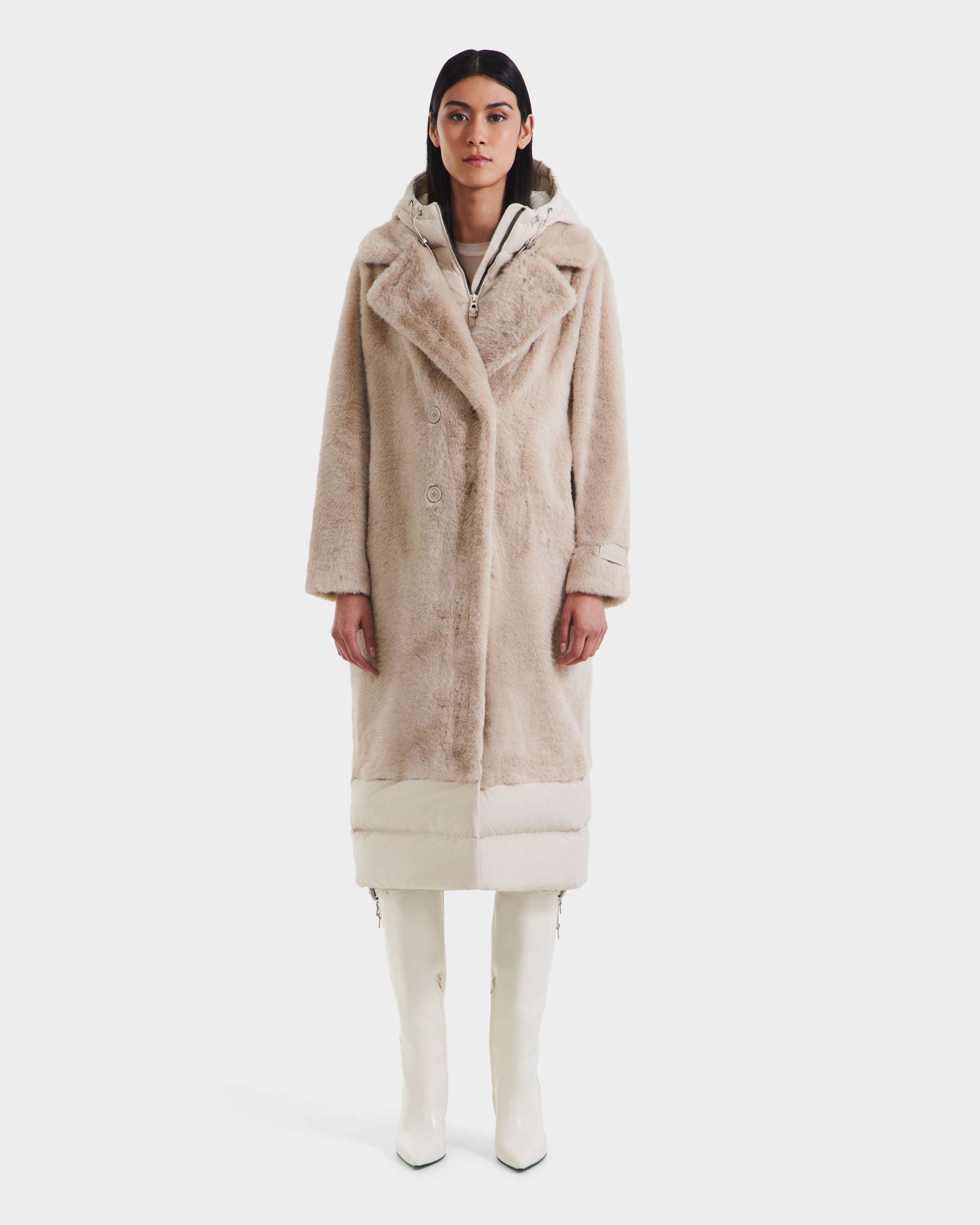 A woman faces forward in the Rudsak SIENA - 8125542 Vanilla faux fur winter coat with a hood, paired with a white inner layer and matching knee-high boots—a cozy look ideal for cold days, set against a plain white background.
